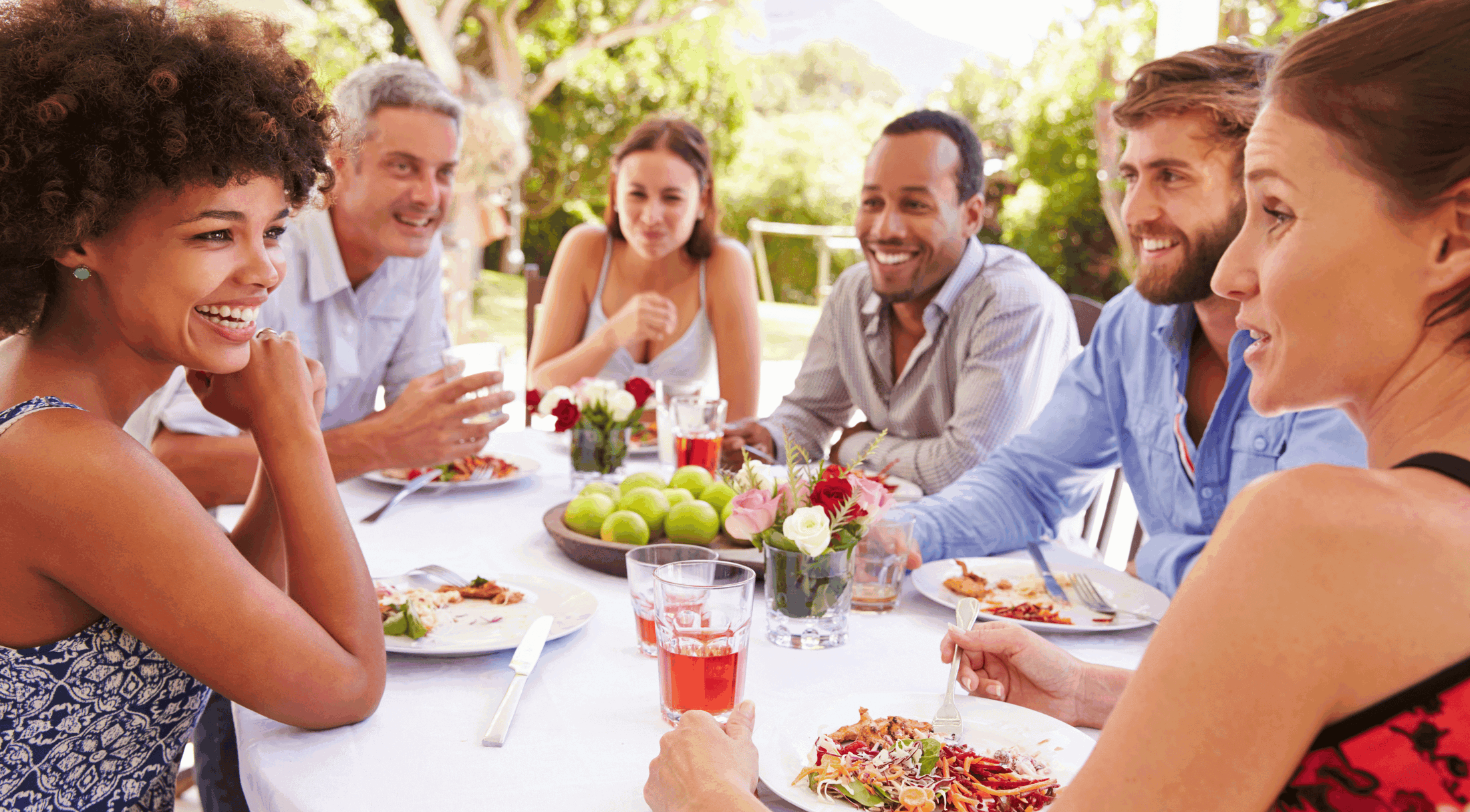 A joyful group of friends enjoying an outdoor meal together at a sunny garden table.