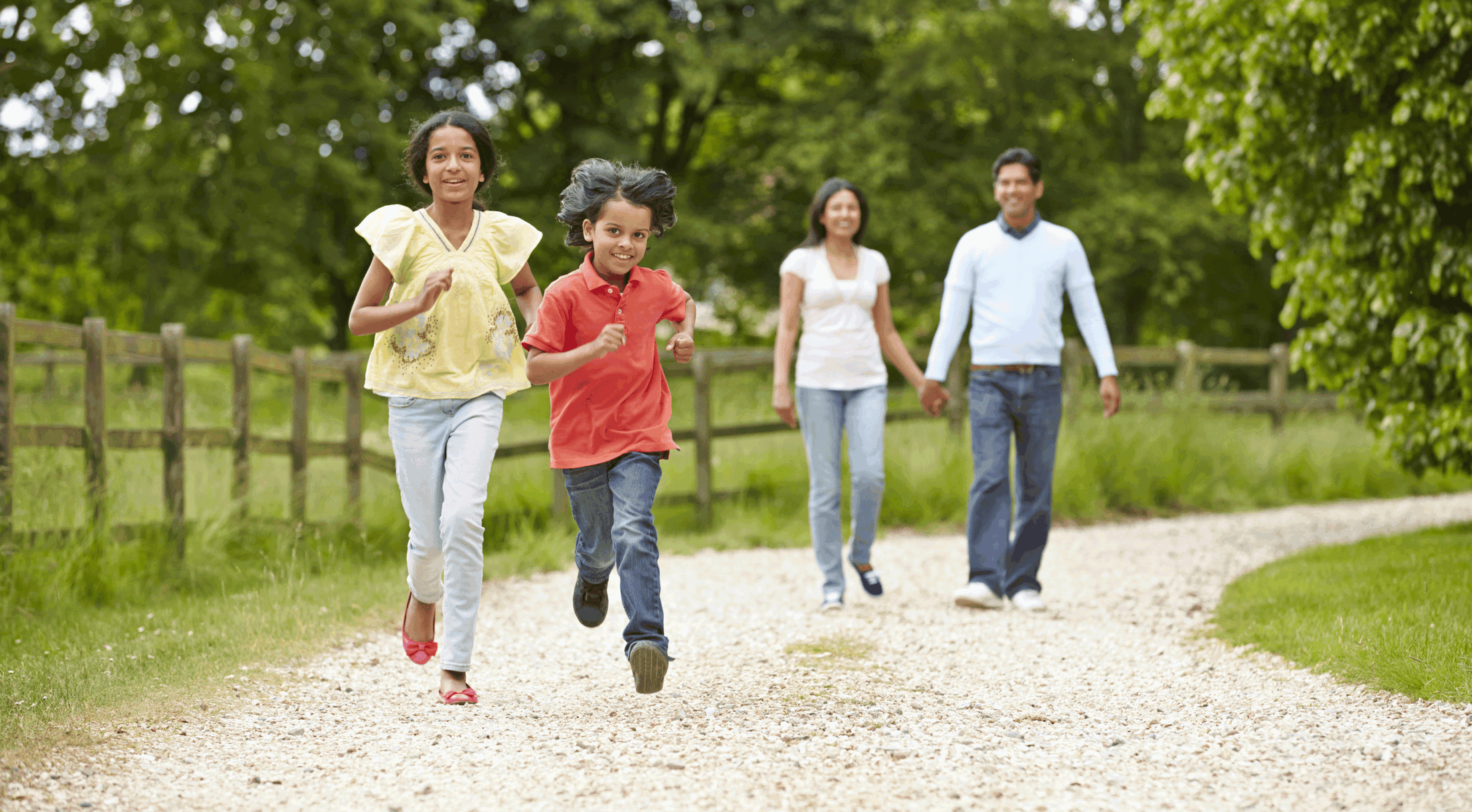 A happy family enjoying a walk and running together on a gravel path in a lush green park.