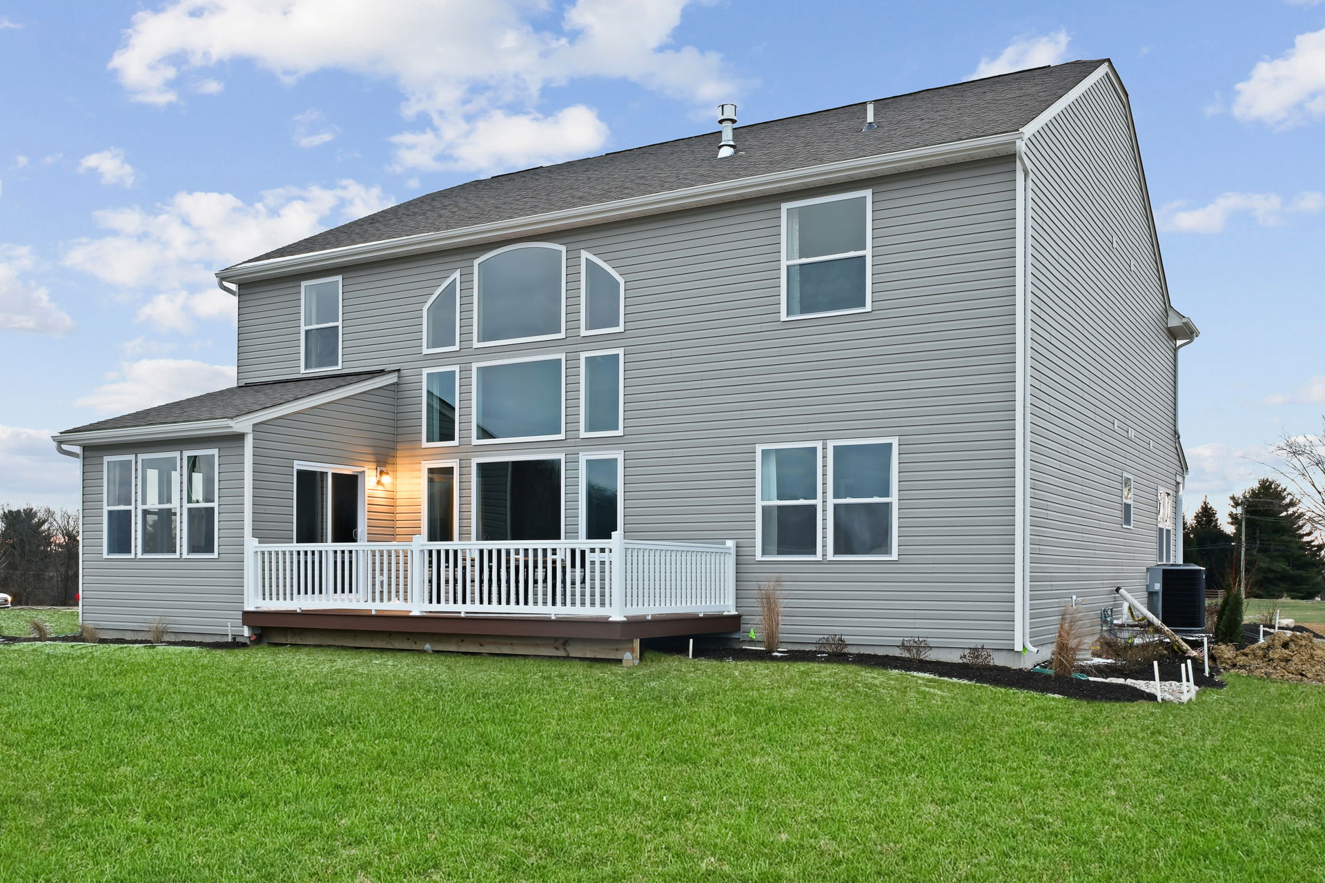Modern two-story house with gray siding and a wooden deck in a spacious backyard.