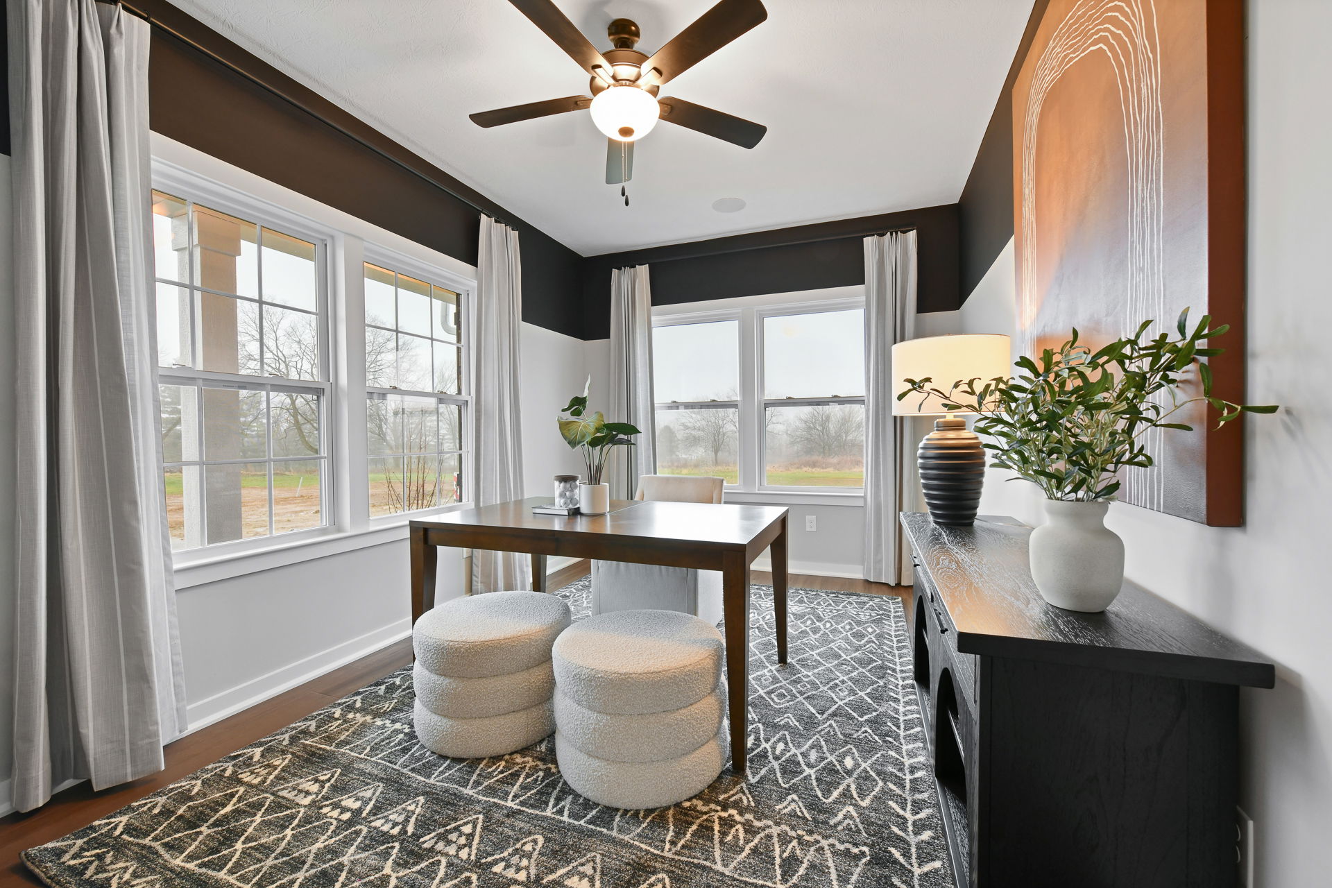 Modern home office with wooden desk, white stools, and large windows illuminating neutral decor.