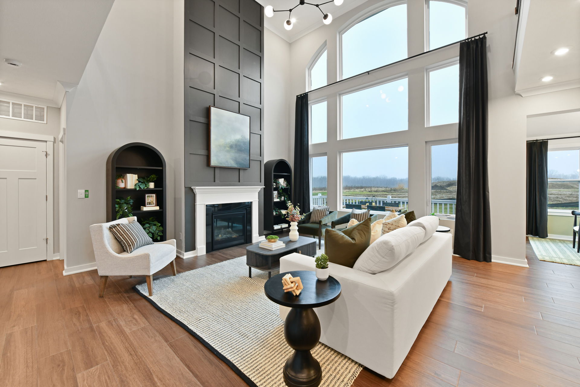 Elegant modern living room with high ceilings, large windows, and cozy fireplace featuring stylish decor and wooden flooring.