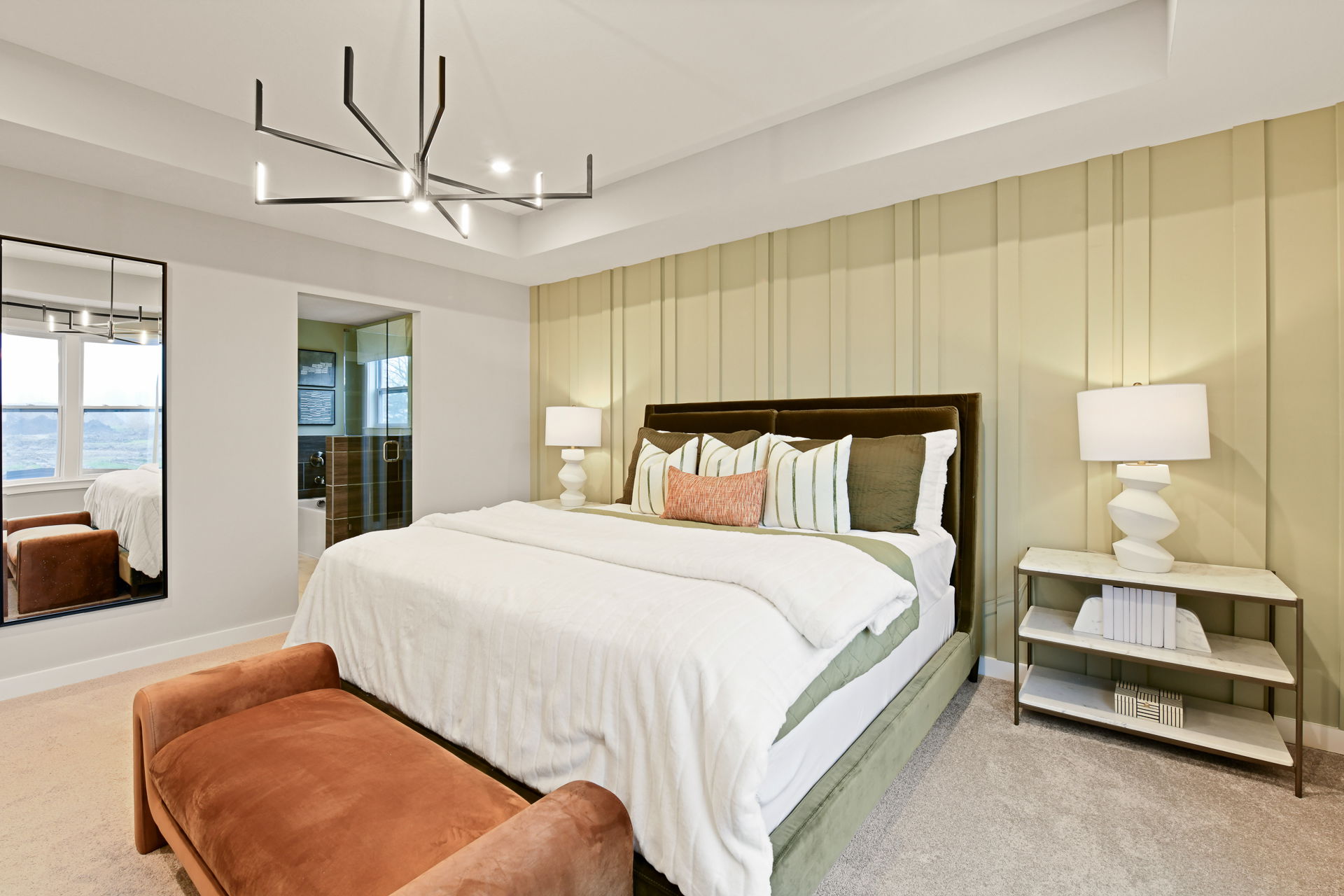 Modern bedroom featuring a large bed with white sheets, decorative pillows, a brown bench, geometric chandelier, and stylish lamps on side tables.