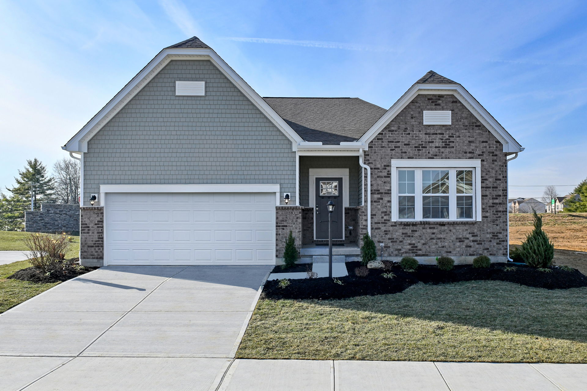 Modern suburban home with gray siding, brick accents, and a double garage under a clear blue sky.