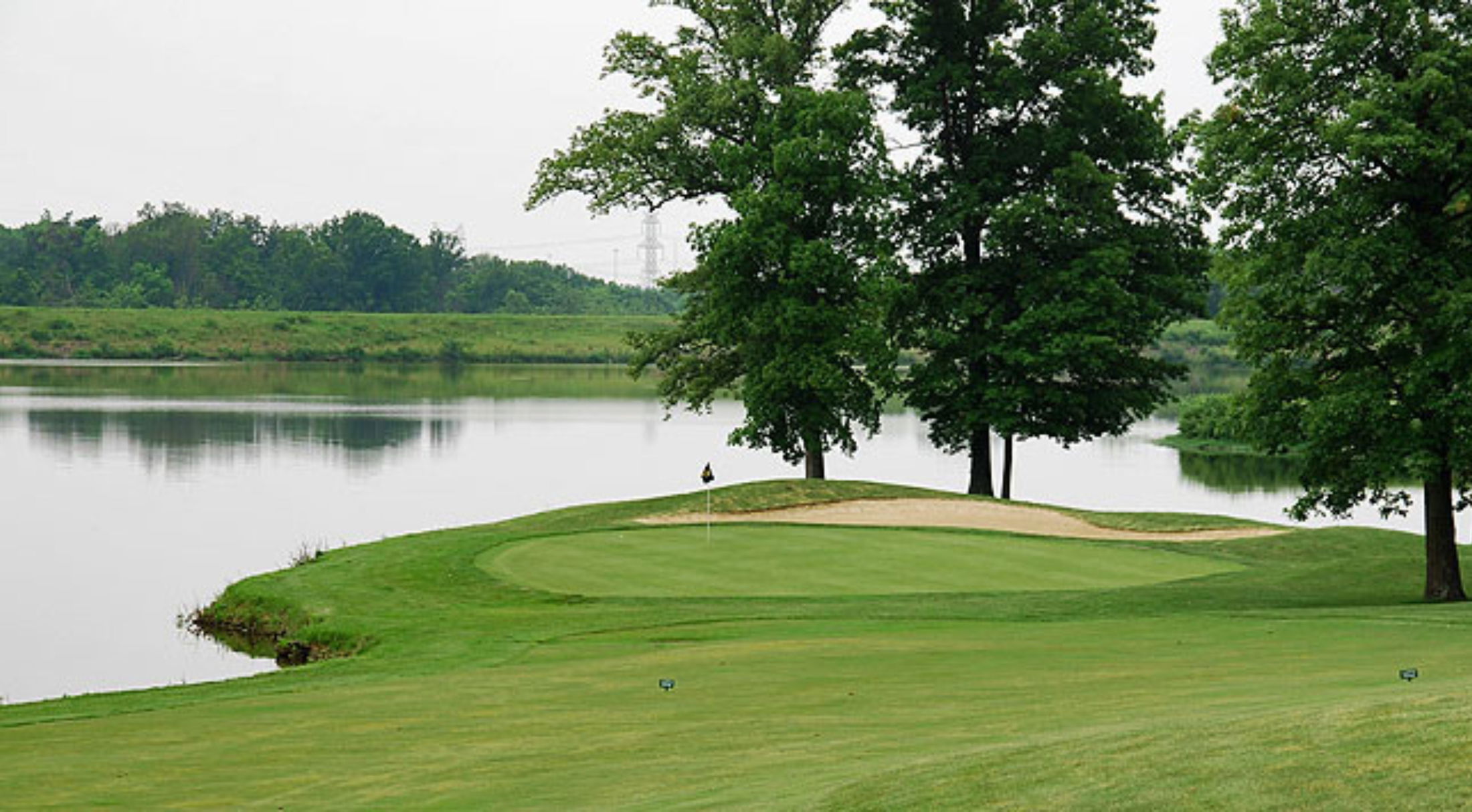 Golf course green with sand bunker and lake surrounded by trees.