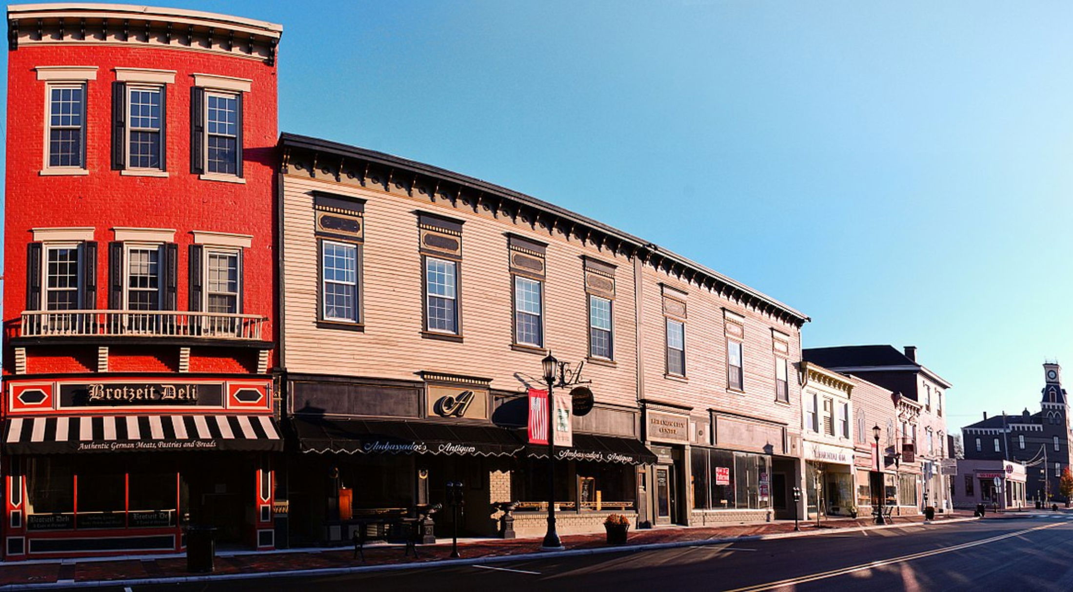 Historic Main Street in downtown Woonsocket, Rhode Island, featuring classic brick and wooden buildings with shopfronts under a clear blue sky.