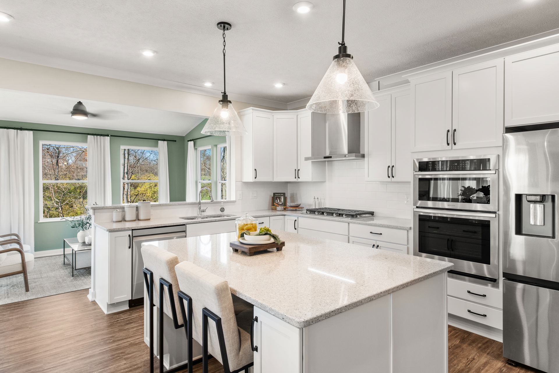 Modern, spacious kitchen with white cabinetry, stainless steel appliances, and a large central island under pendant lighting.