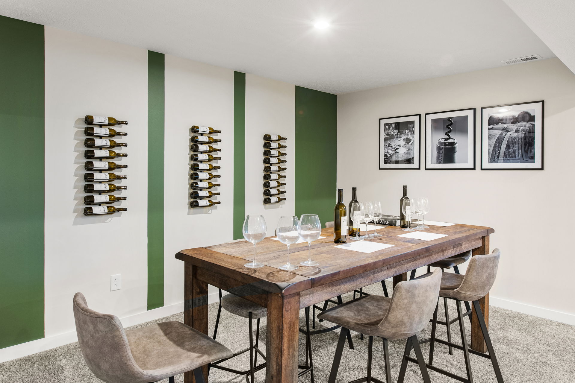 Modern wine tasting room with wall-mounted bottle racks, a rustic wooden table set with wine glasses, and framed wine-themed artwork.
