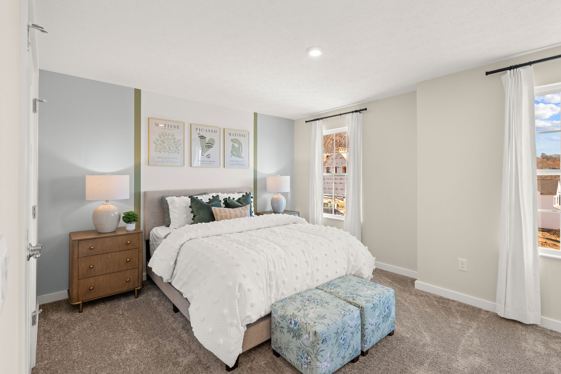 Modern bedroom with a cozy bed, elegant nightstands, wall art, and large windows offering natural light.