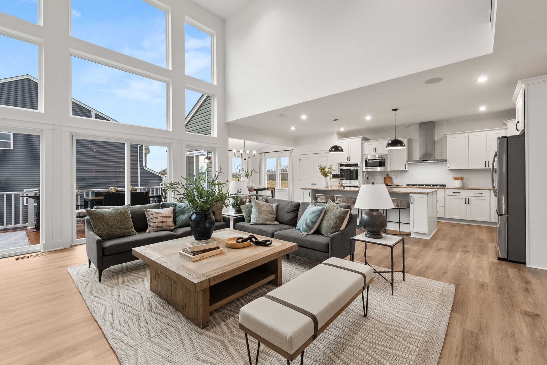 Modern open-concept living room and kitchen with high ceilings, large windows, and stylish furnishings.
