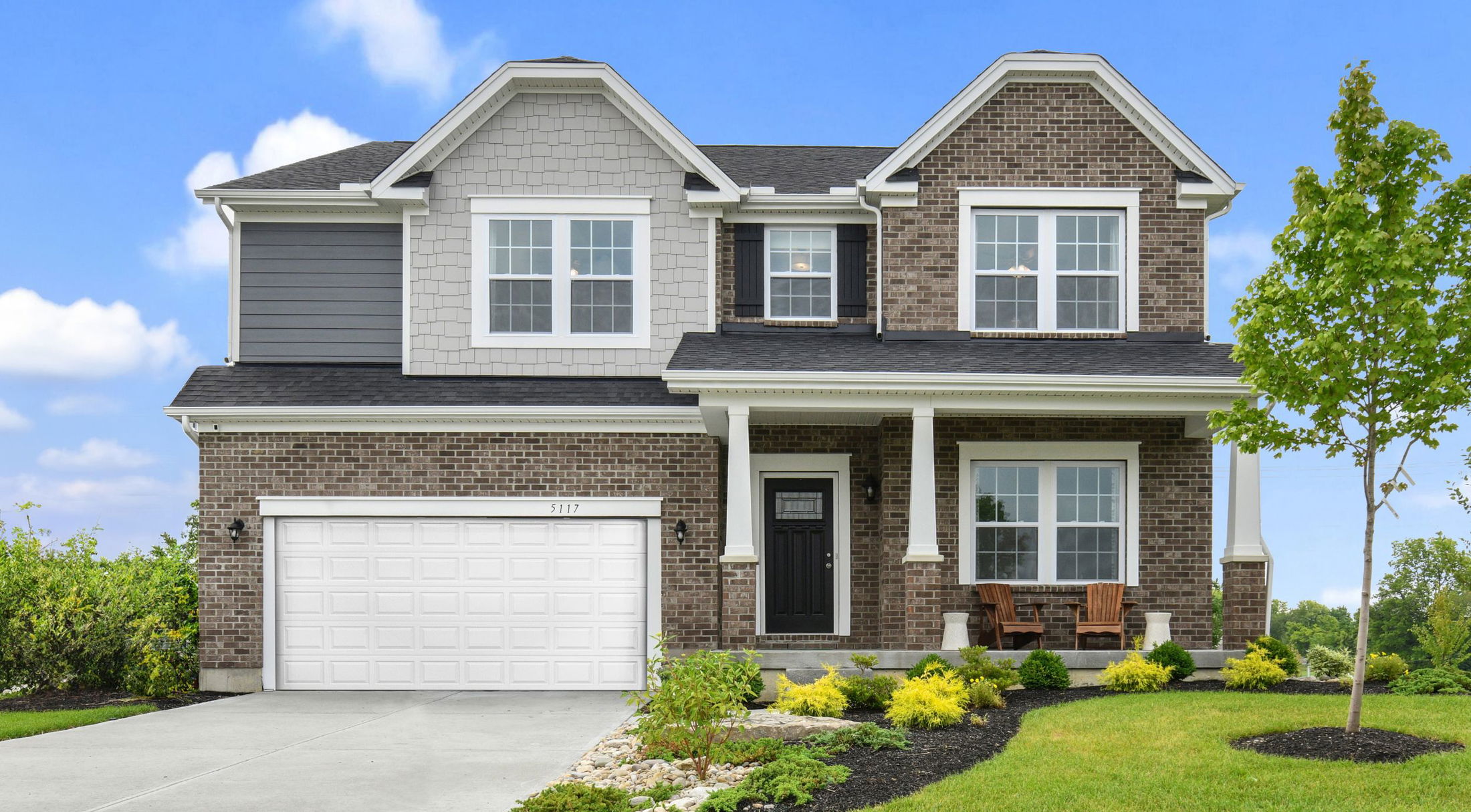 Beautiful two-story brick house with white trim and a landscaped front yard under a clear blue sky.