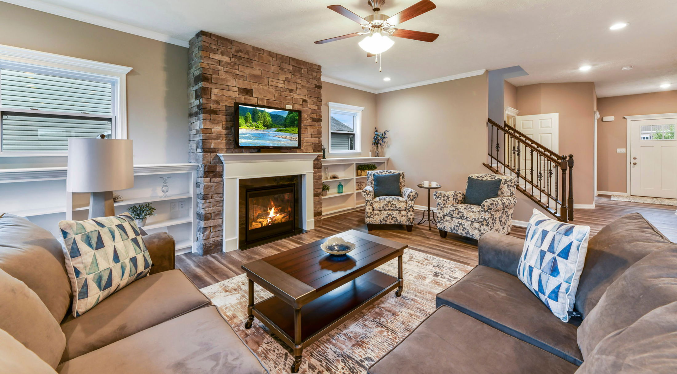 Modern living room featuring a cozy stone fireplace, stylish furniture, and a ceiling fan for a welcoming ambiance.