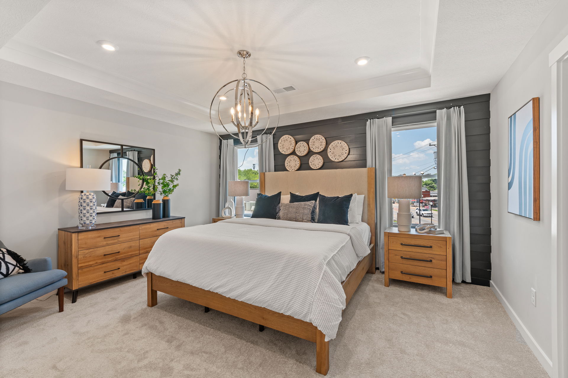 Modern bedroom with wooden furniture, elegant bedding, decorative wall plates, and a stylish chandelier.
