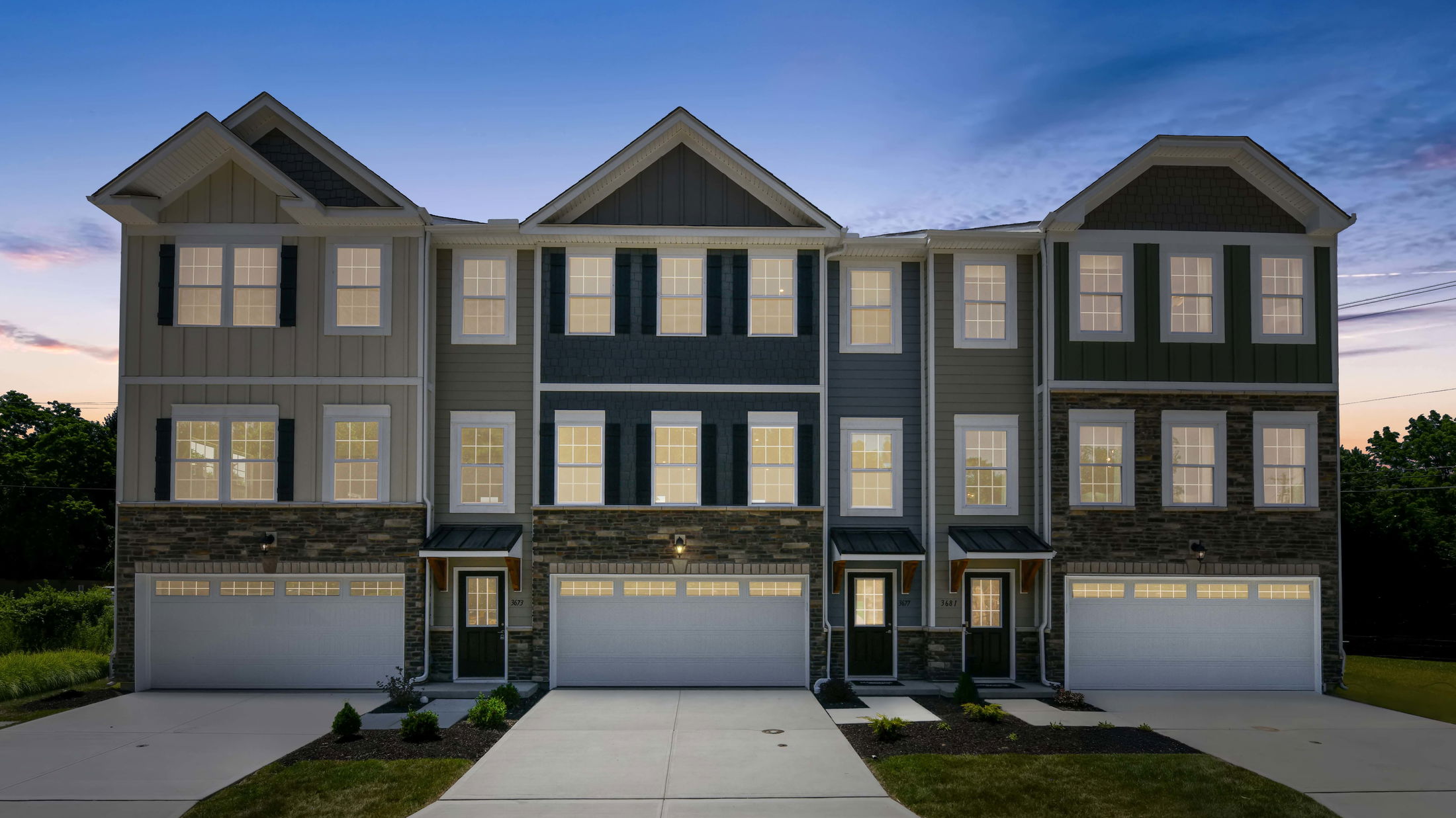 Modern townhouse exterior at dusk with lit windows and dual garages, showcasing elegant design and curb appeal.