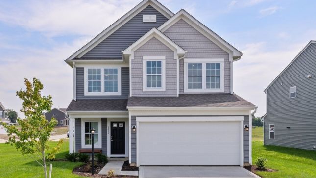Two-story gray house with a white garage door, surrounded by green grass and a small tree.