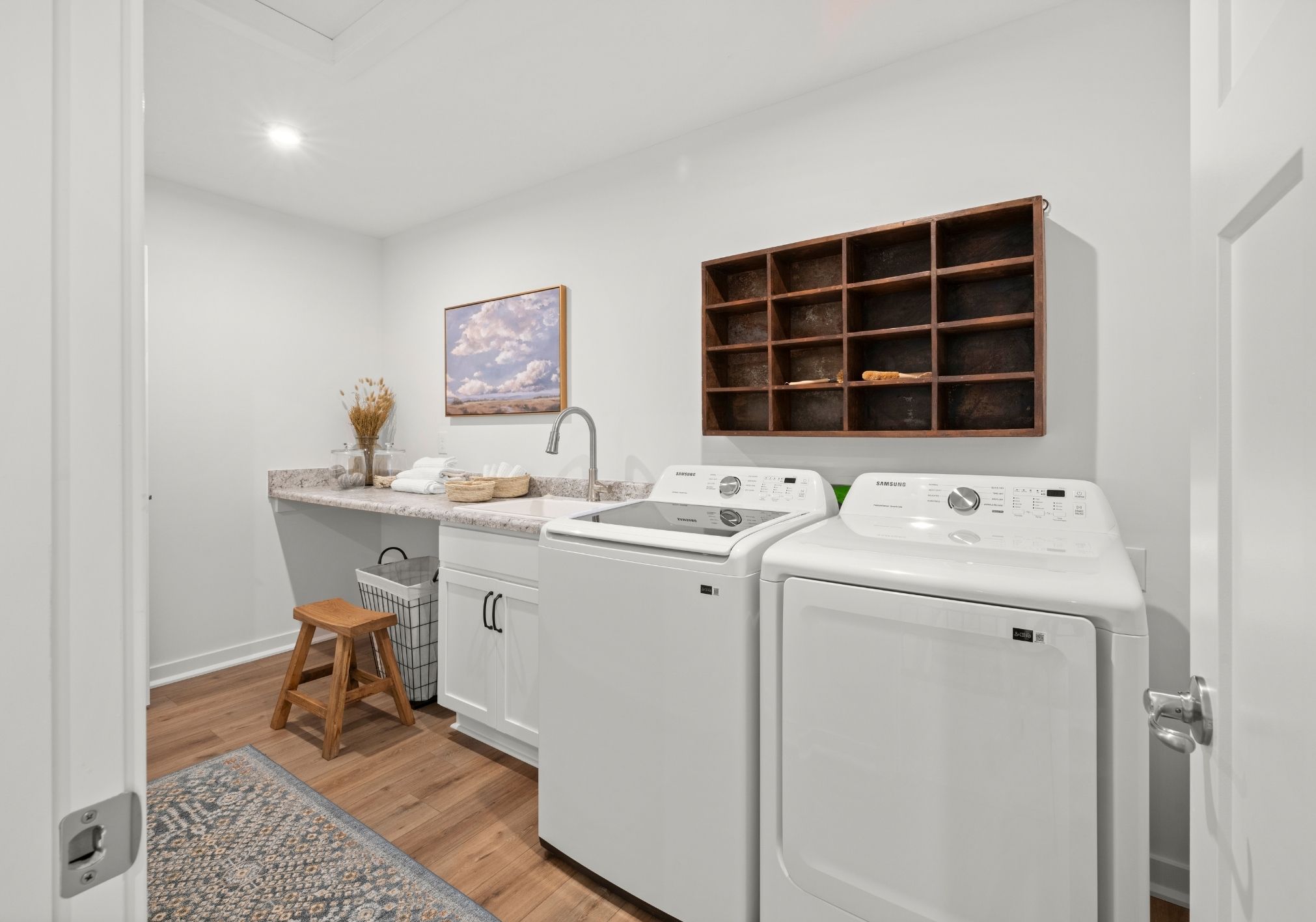 A modern laundry room featuring white appliances, a wooden shelf, and a decorative painting on the wall.