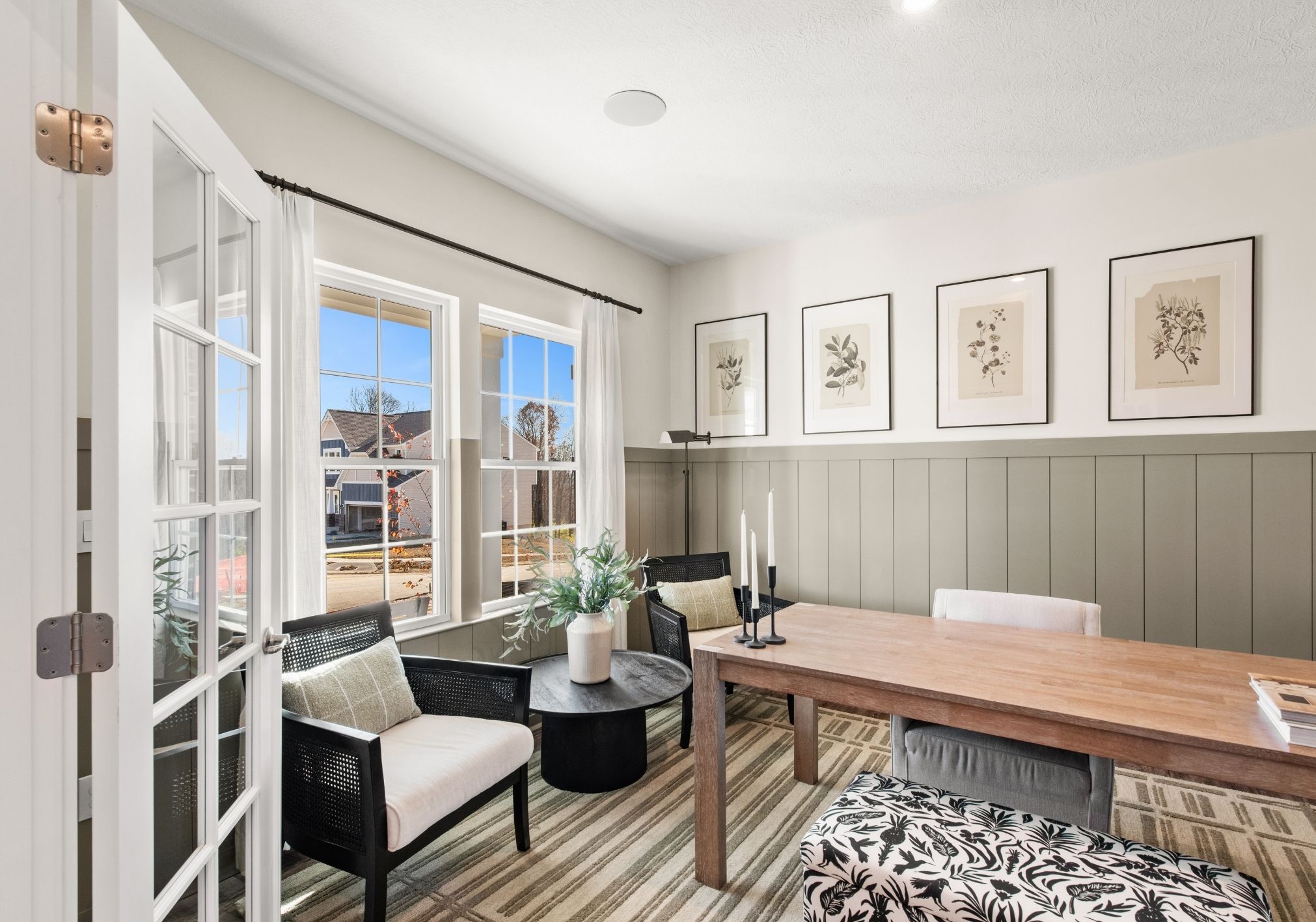 A bright dining area with a wooden table, black chairs, and framed botanical prints on the wall.