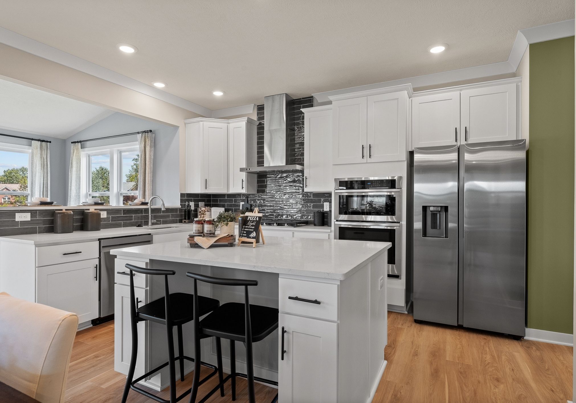 Modern kitchen with white cabinetry, stainless steel appliances, and a central island with black seating.