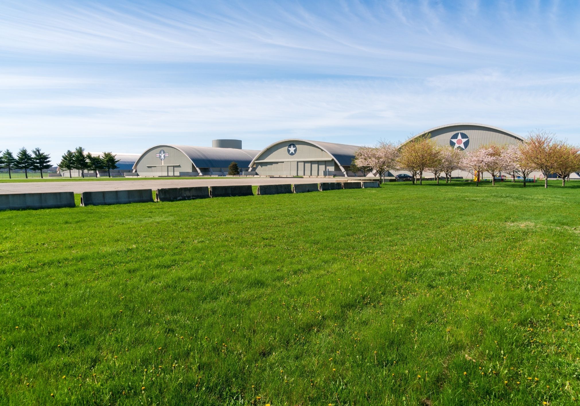 A grassy field in front of large, curved metal buildings with star insignias and a clear blue sky.