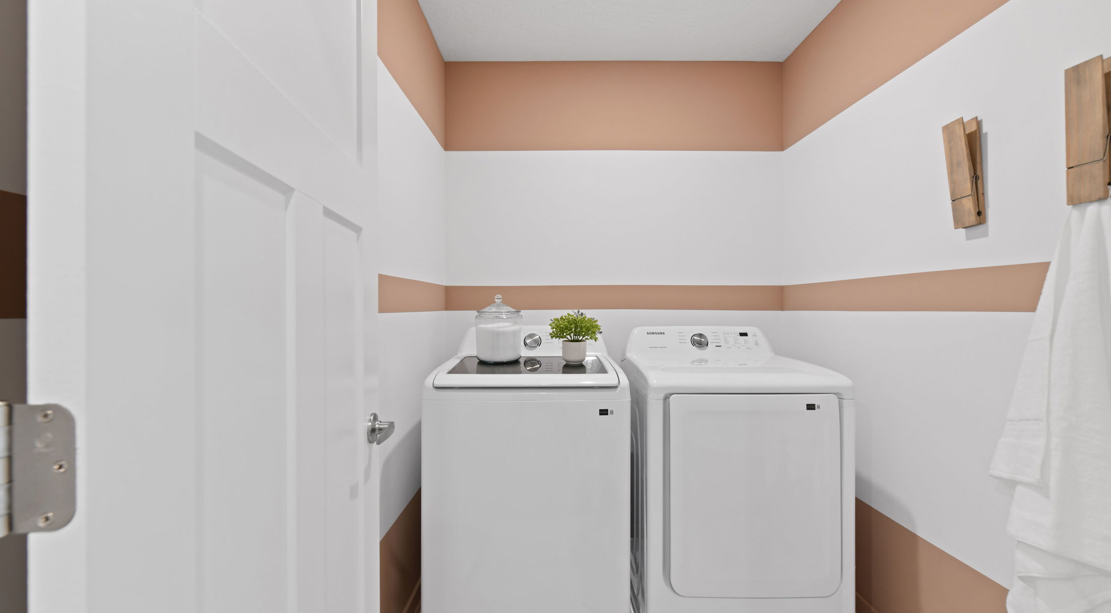 Modern laundry room with white washing machine and dryer, beige-white striped walls, and decorative accents.