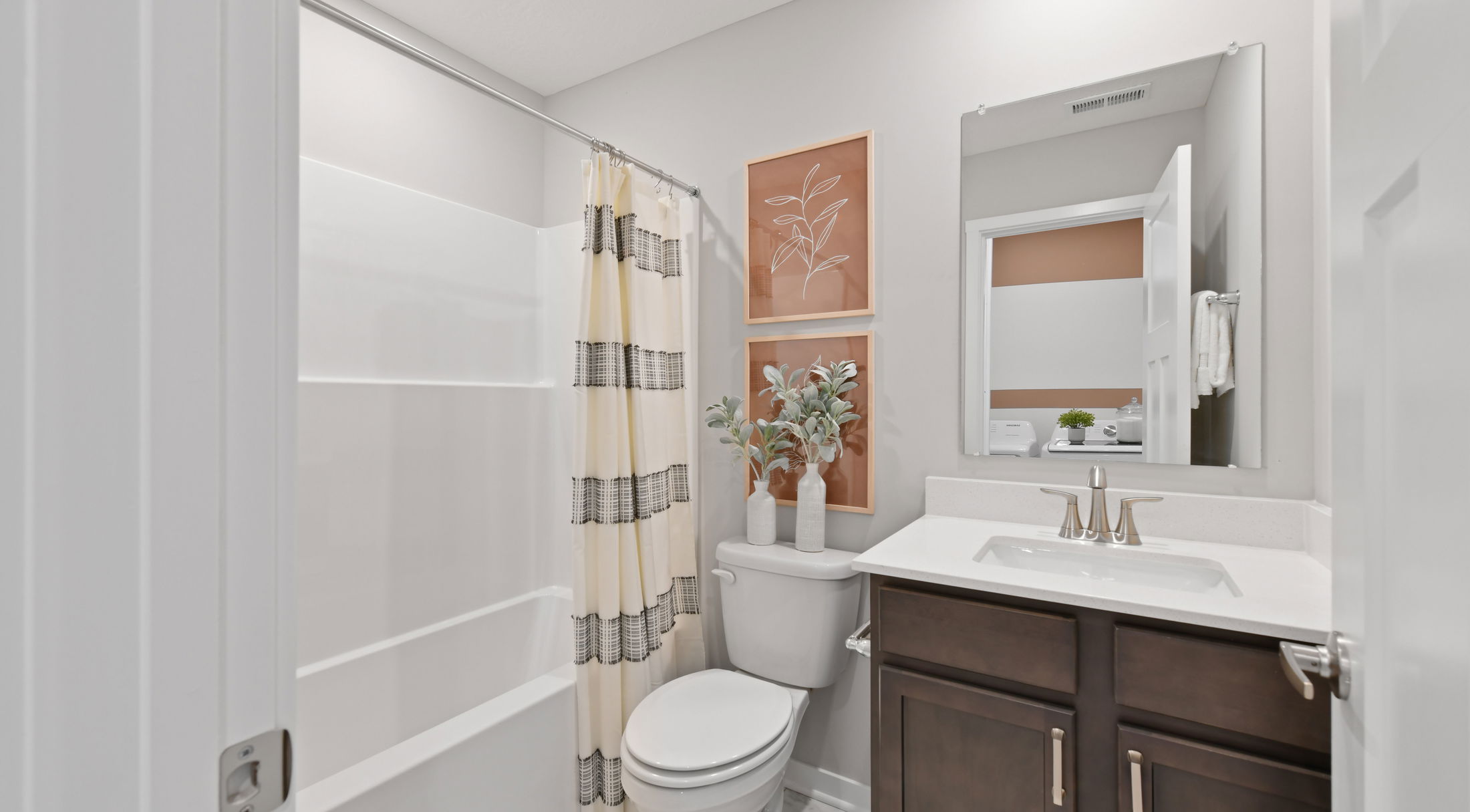 Modern bathroom with a white bathtub and shower curtain, dark wood vanity, framed art, and potted plants for a stylish, clean design.