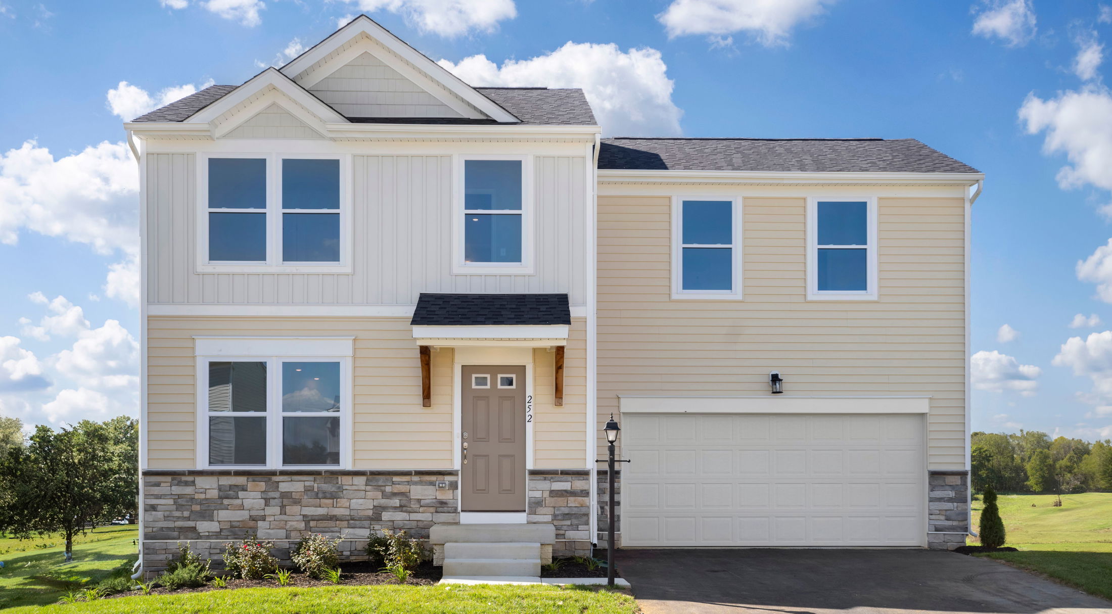 Modern two-story beige house with a double garage and a well-maintained front yard under a clear blue sky.
