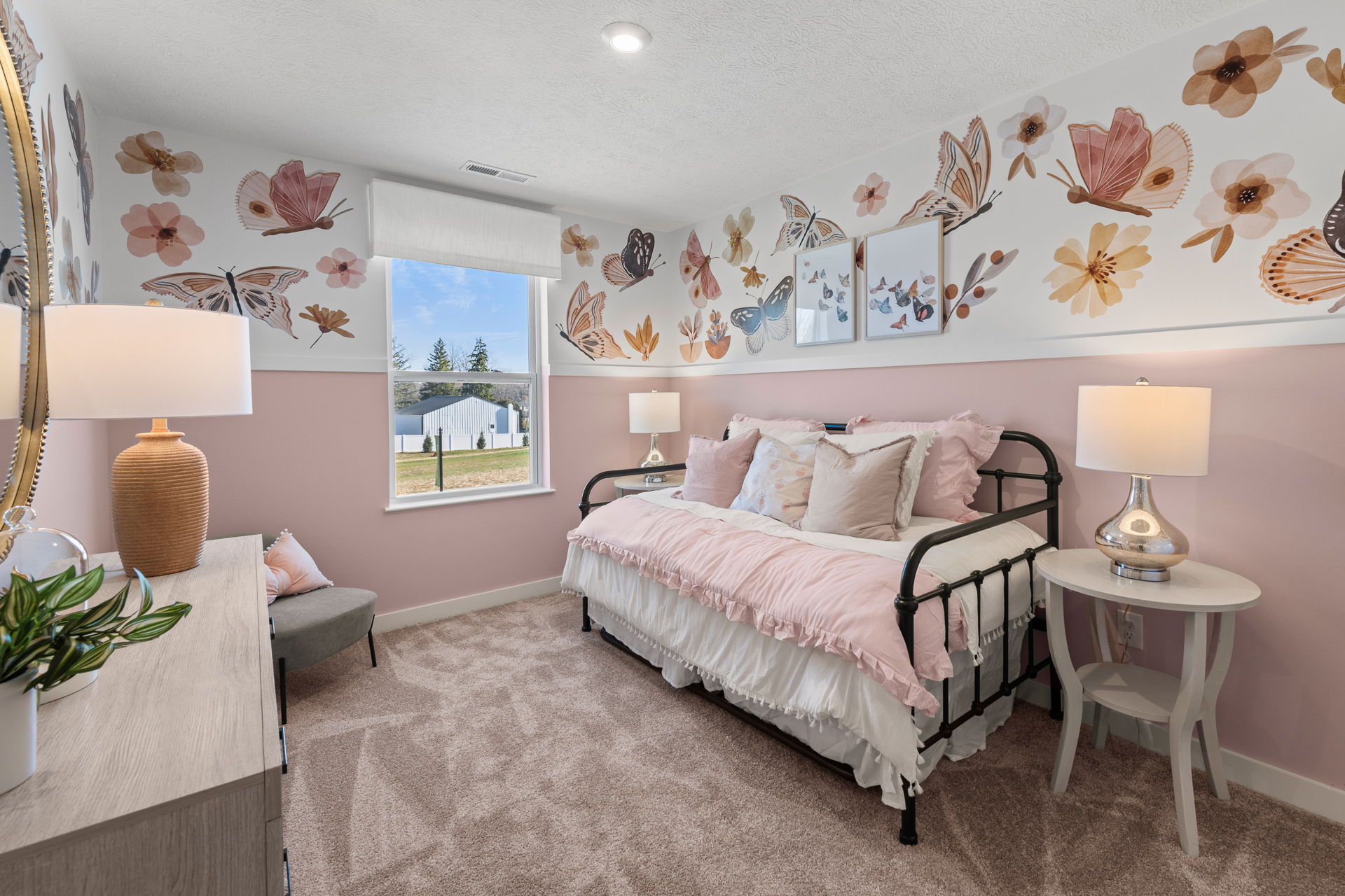 A cozy, pink-themed bedroom with butterfly and floral wall art, a metal bed frame, and soft lighting, creating a charming and inviting atmosphere.