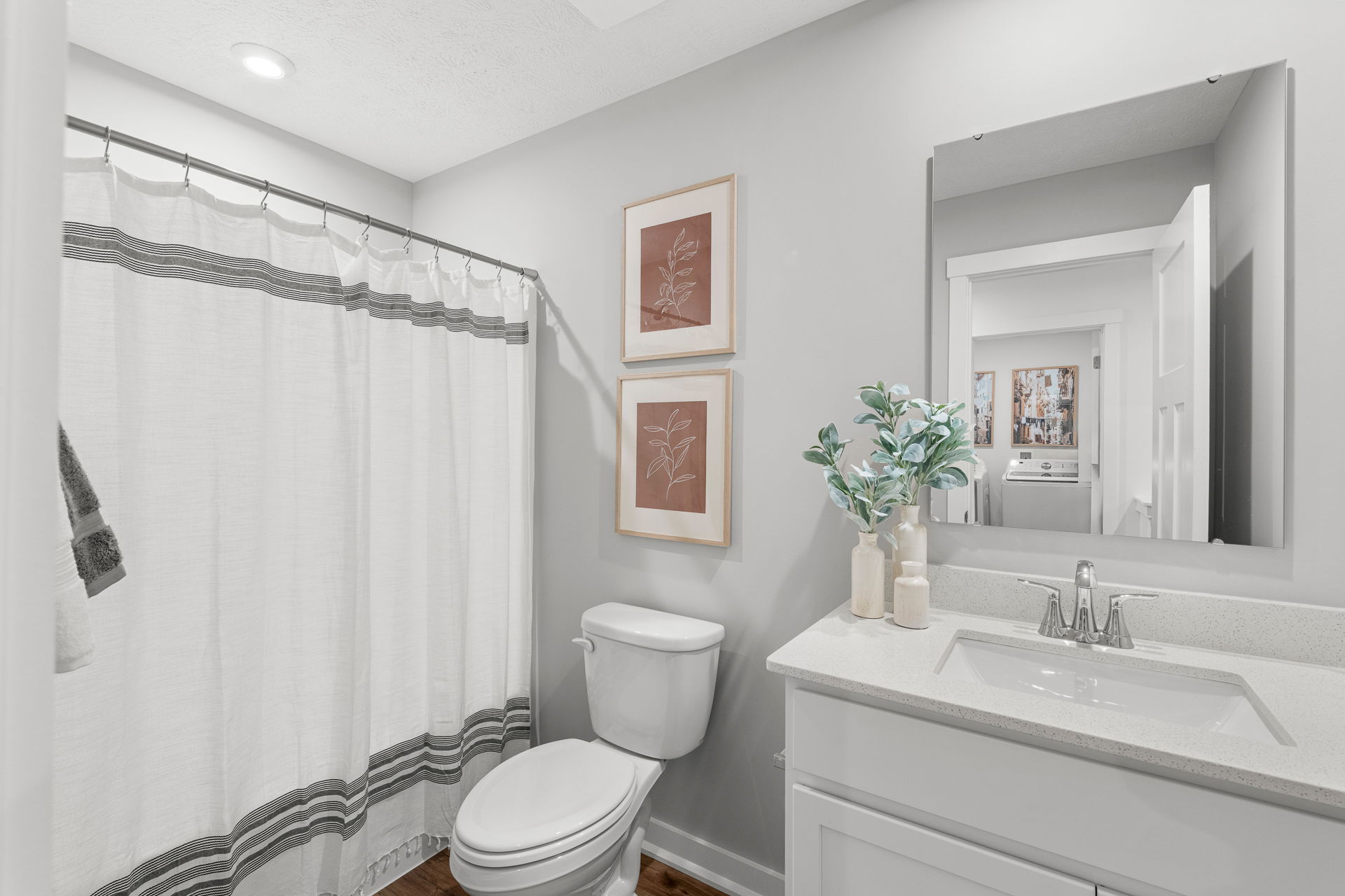 Minimalist bathroom with white shower curtain, modern vanity, decorative plants, and framed botanical art.