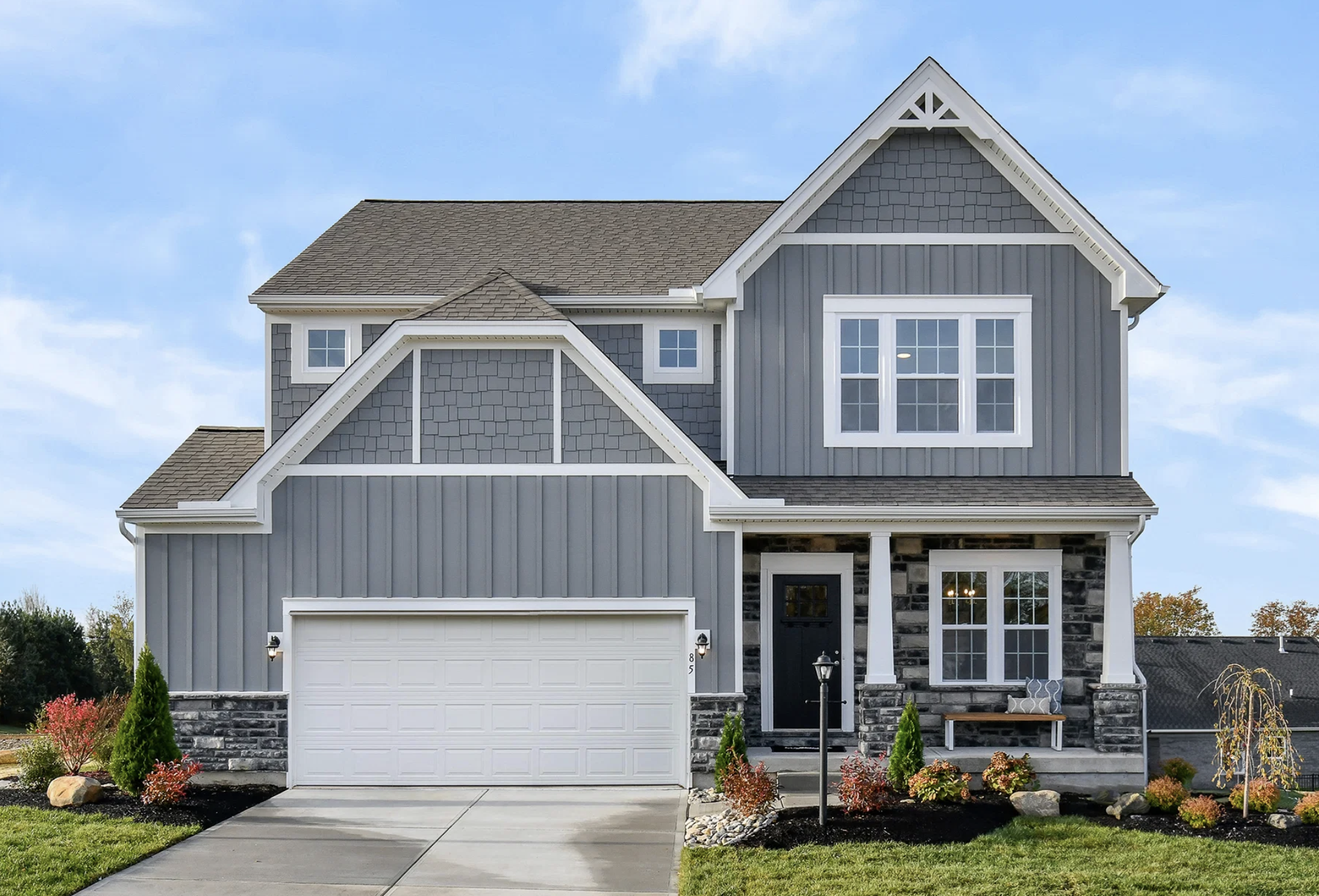A modern gray house with stone accents, featuring a two-car garage and landscaped front yard.