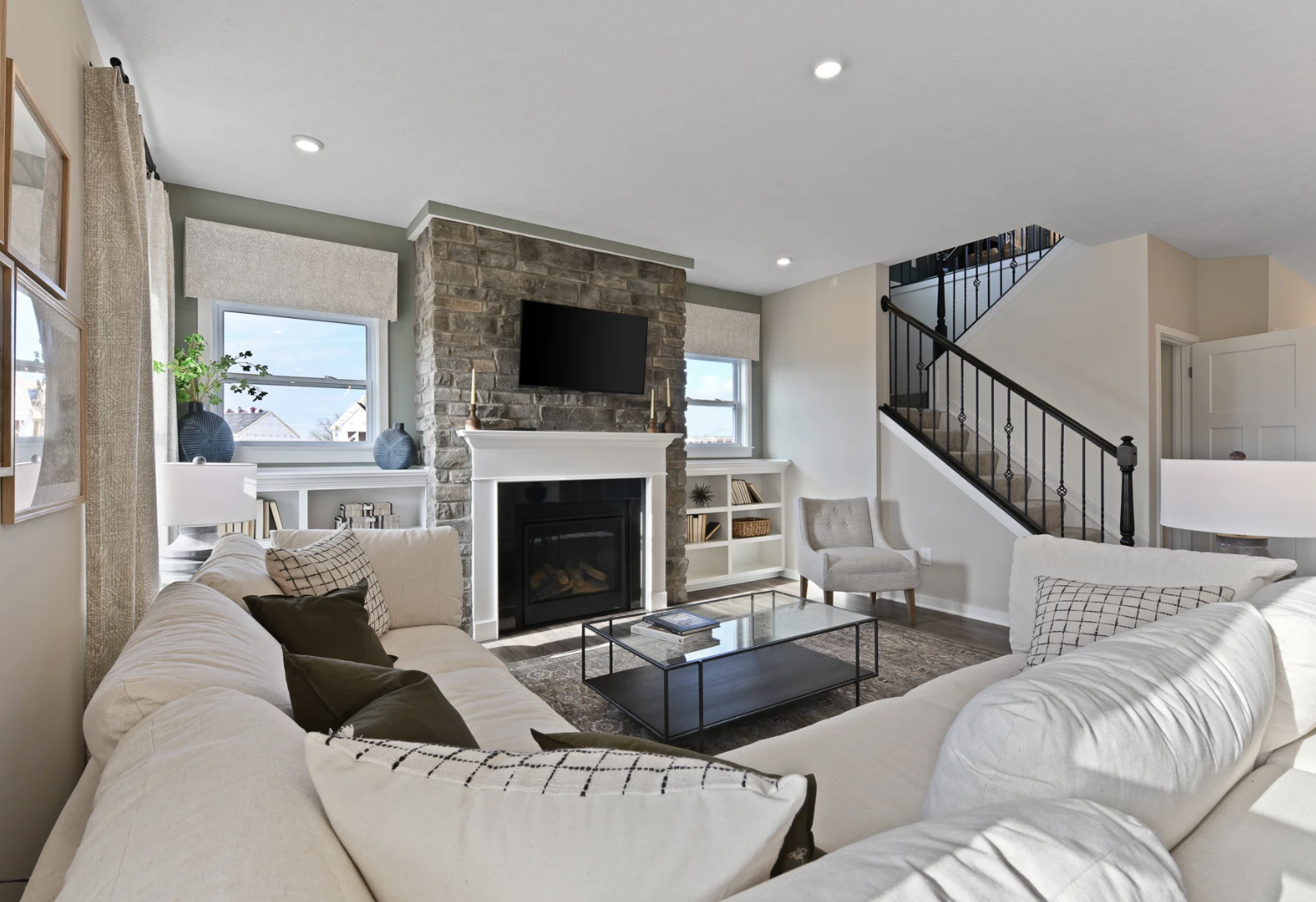 A modern living room featuring a stone fireplace, a white sectional sofa, and a staircase.