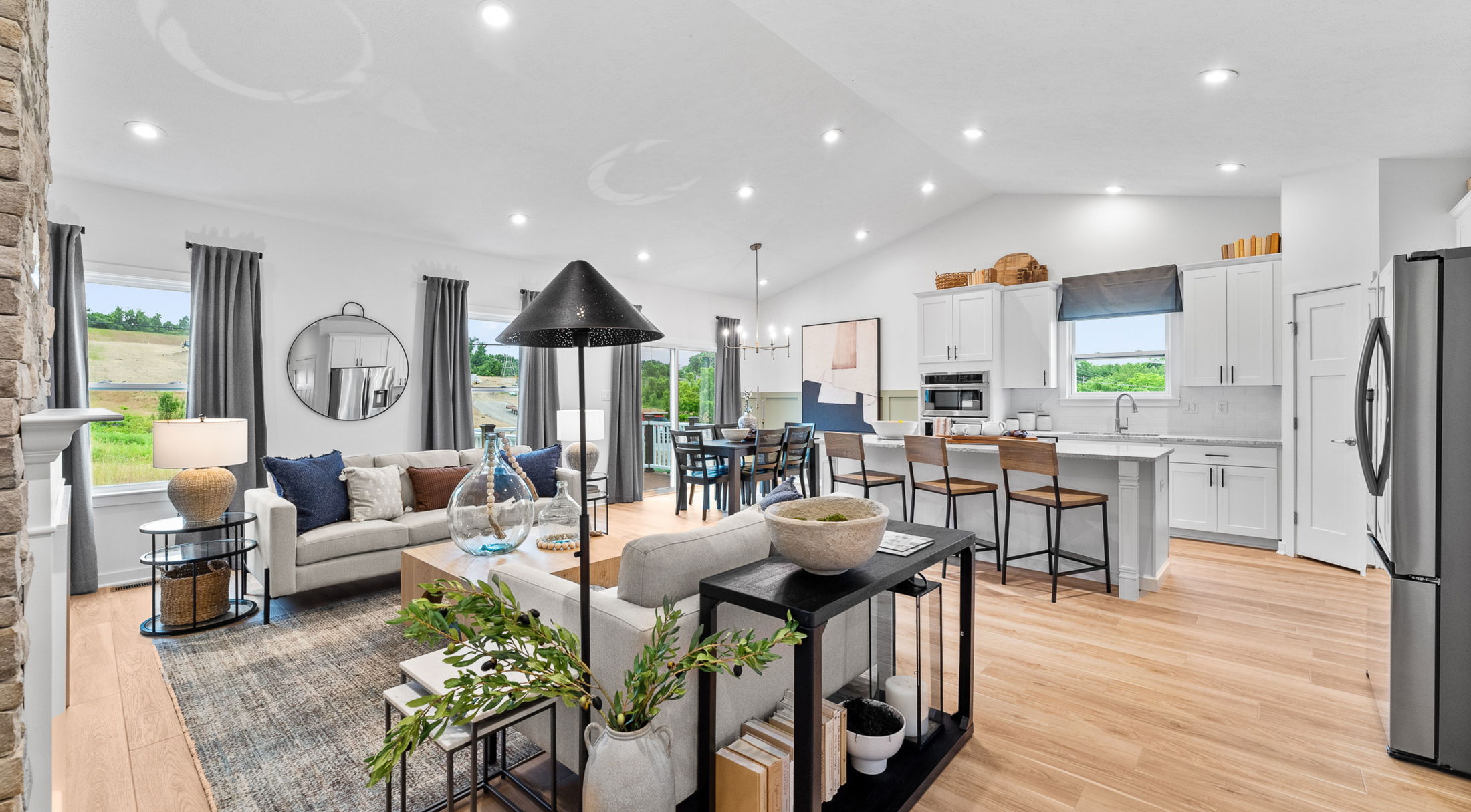 Modern open-concept living room and kitchen with stylish decor, featuring a gray sofa, round mirror, and wooden accents.