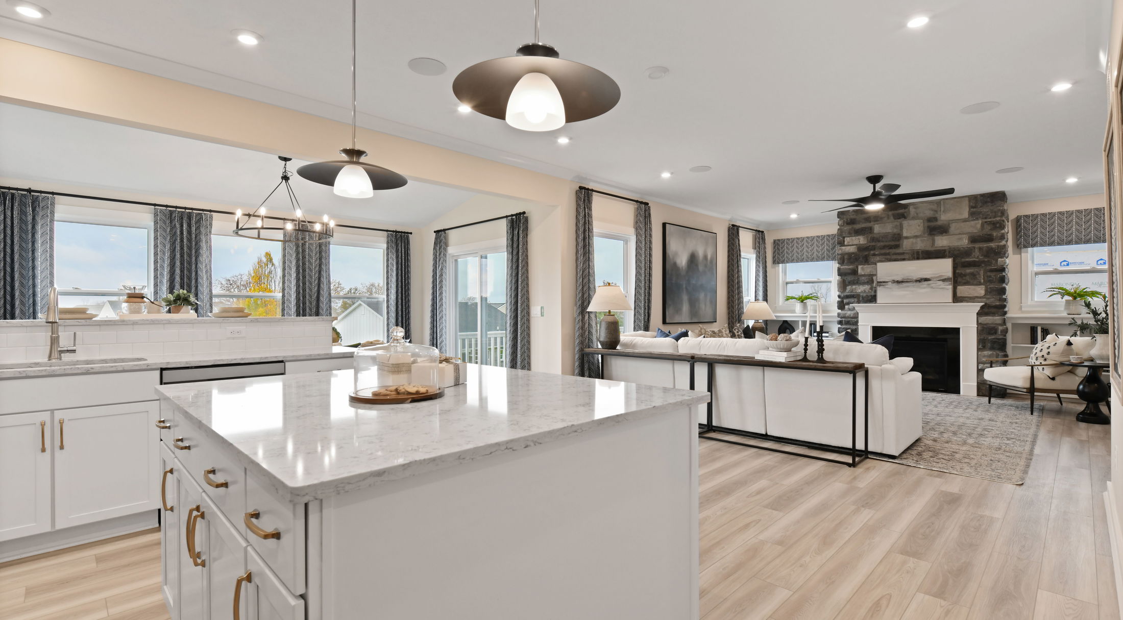 Modern open-concept living room and kitchen with white cabinetry, stone fireplace, and contemporary lighting.