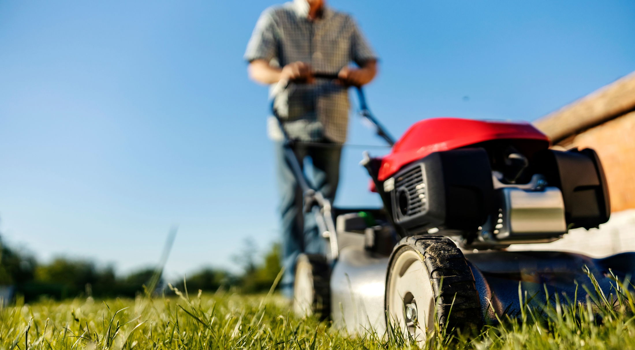 A person mowing a lawn with a red and black lawnmower on a sunny day.