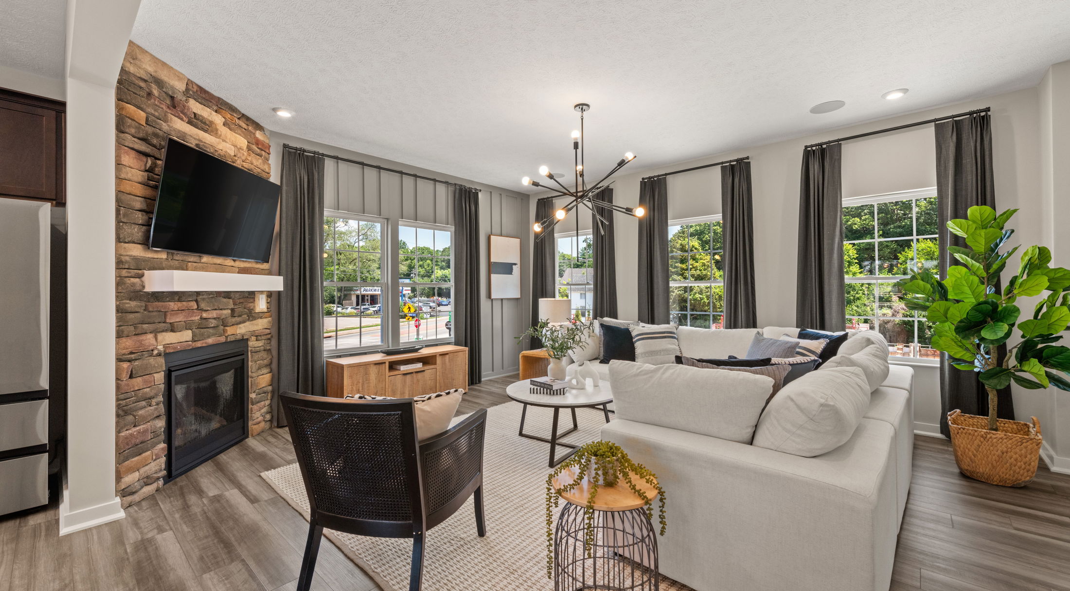 Modern living room with a white sectional sofa, a stone fireplace, large windows, and contemporary lighting.