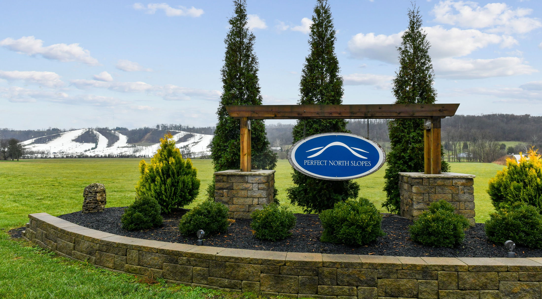 Signage for Perfect North Slopes with snow-covered ski hills in the scenic background.