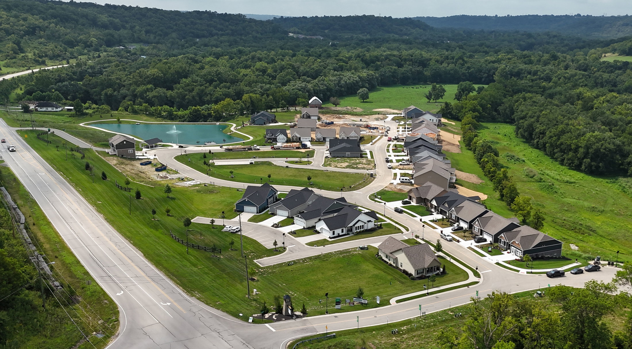 Aerial view of a residential neighborhood with a pond, surrounded by greenery and under construction homes.