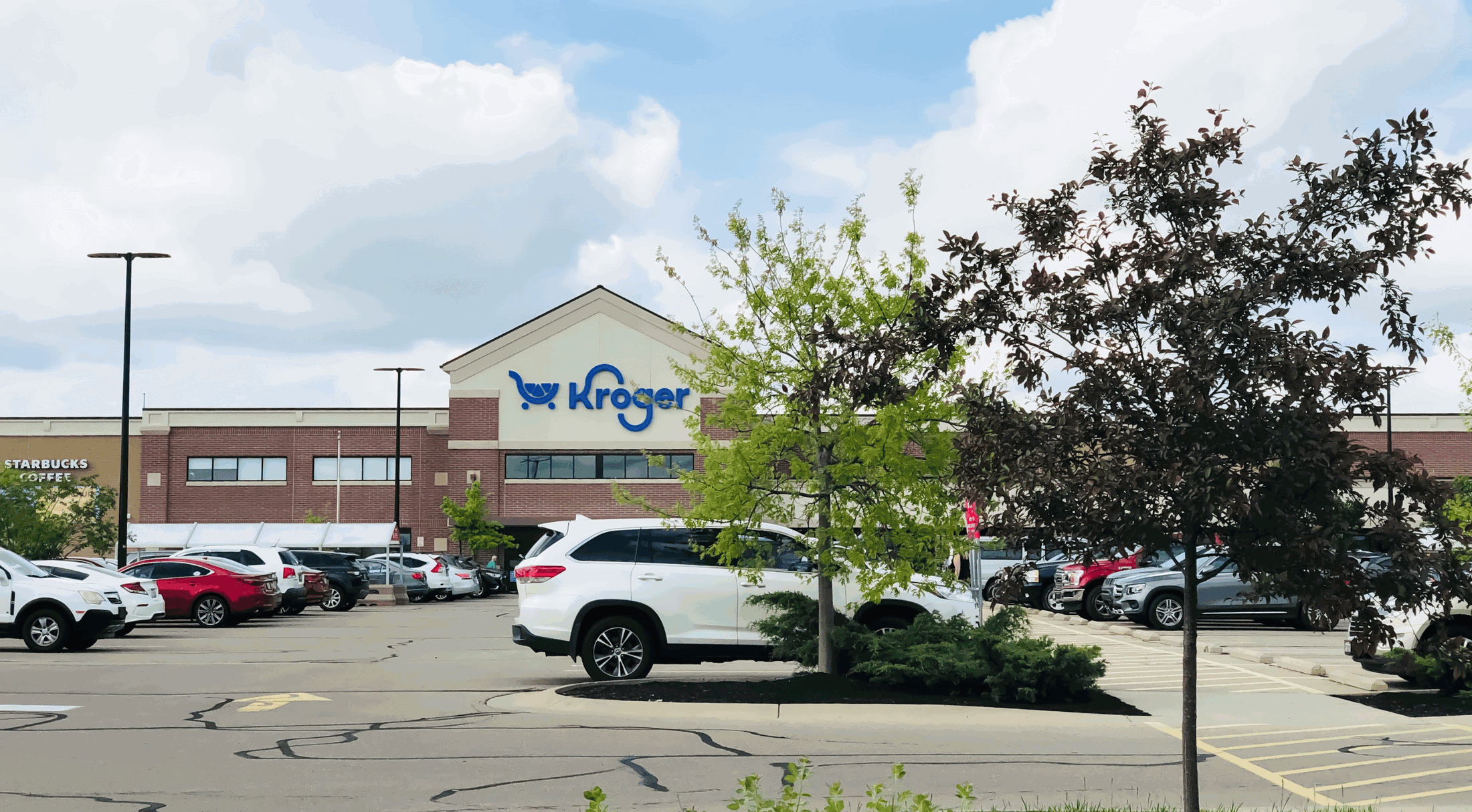 Front view of a Kroger store with a parking lot and multiple cars under a partly cloudy sky.