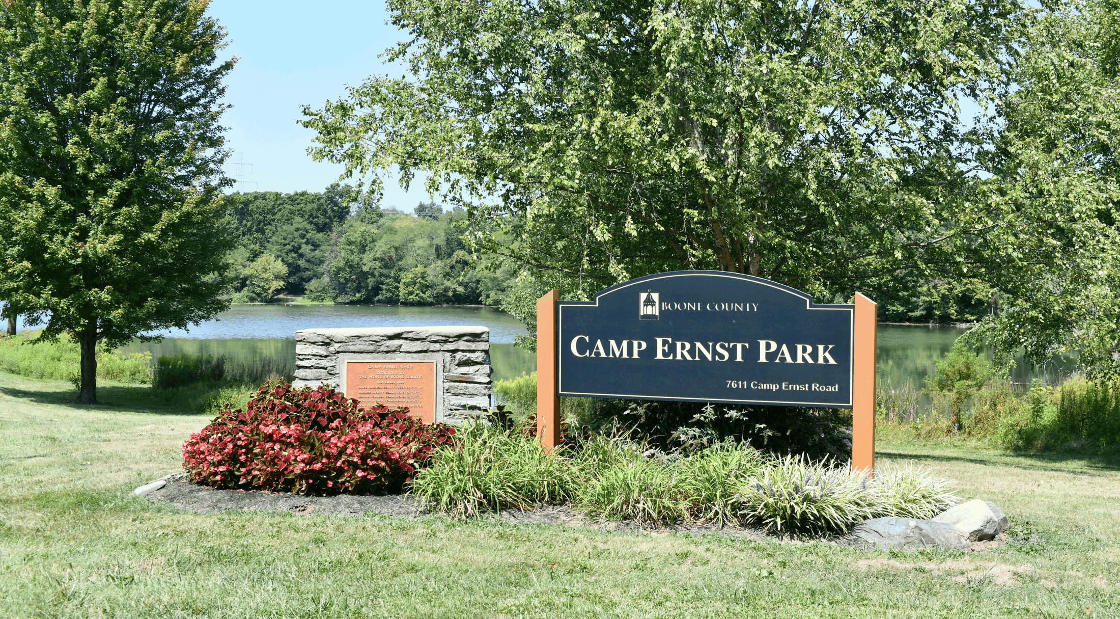 Sign for Camp Ernst Park in Boone County, surrounded by lush greenery and a scenic lake backdrop.