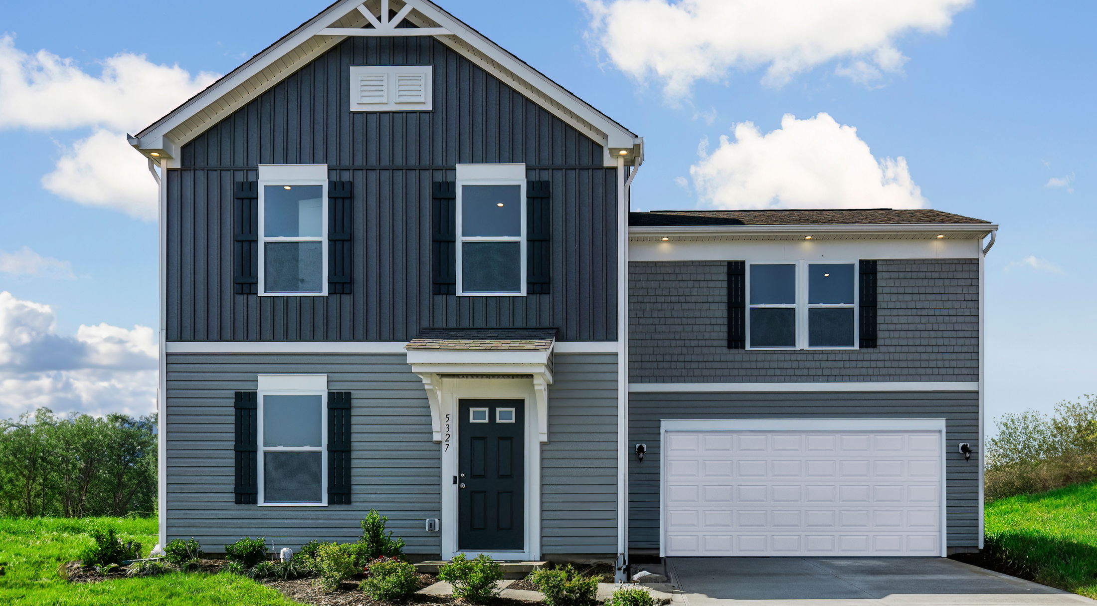 Two-story modern gray house with a white garage door and gabled roof under a blue sky.