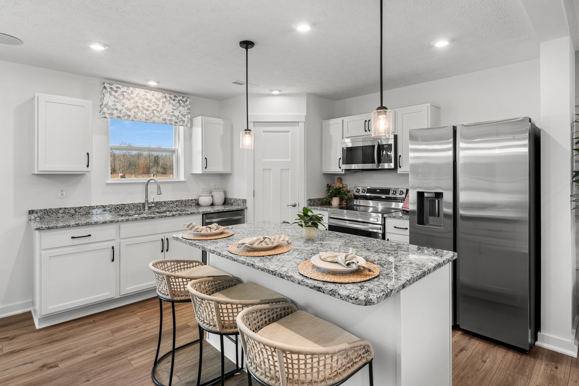 Modern kitchen with granite countertops, white cabinets, stainless steel appliances, and wicker barstools at a center island.