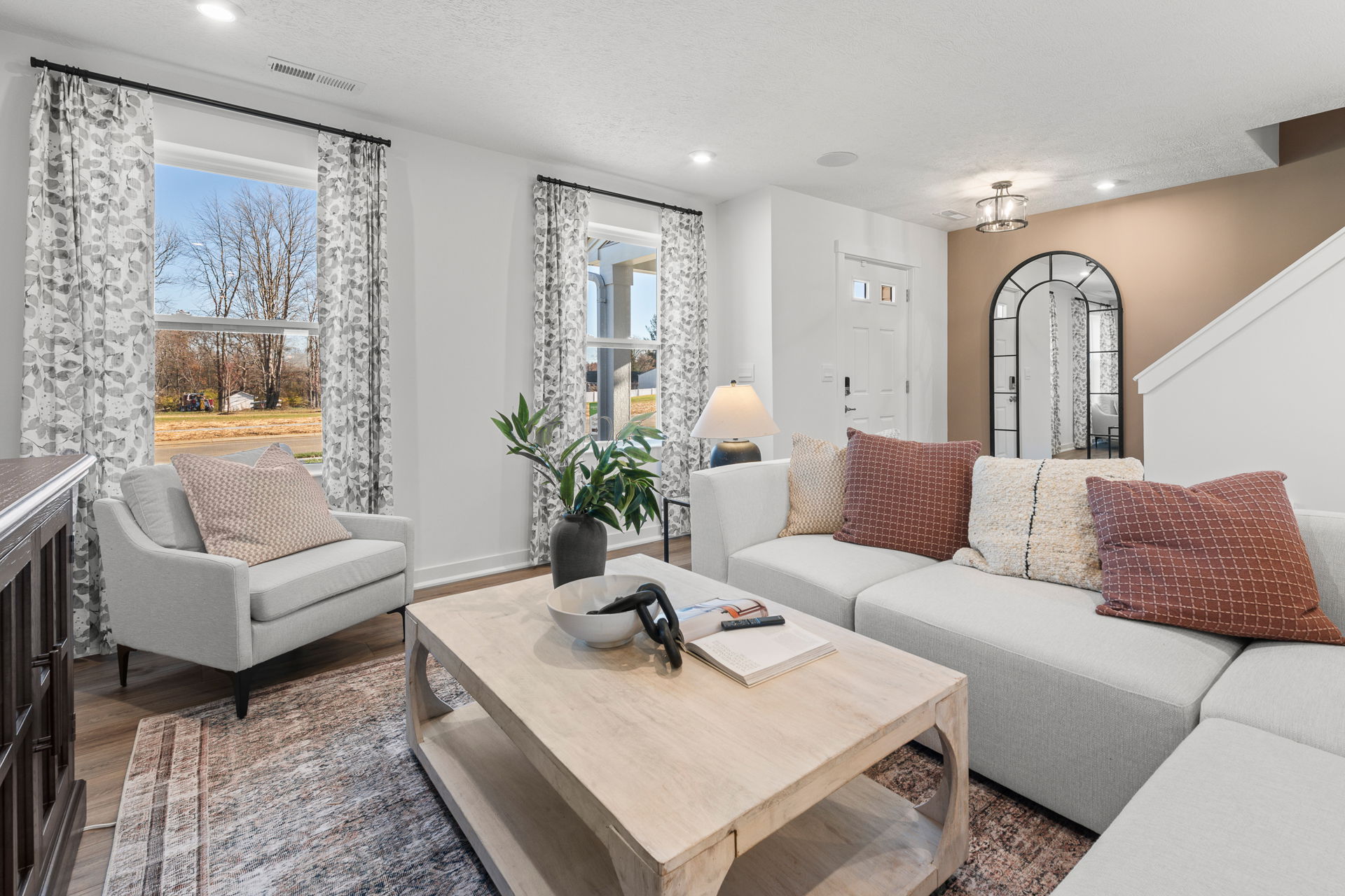 Modern living room with a cozy white sectional sofa, patterned pillows, large mirror, and stylish decor in a well-lit space.