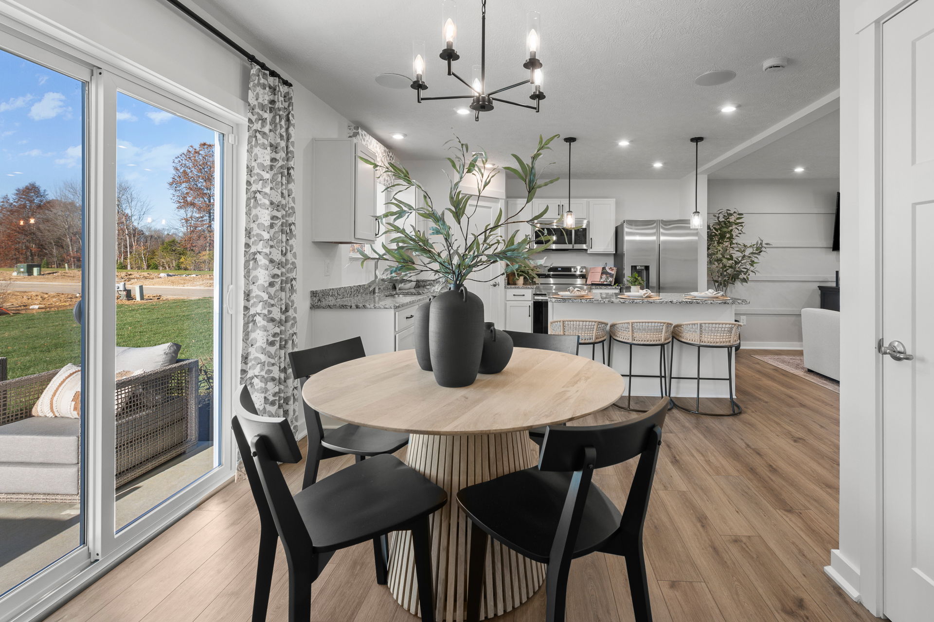 Modern dining area with a round wooden table, black chairs, and a view into the stylish kitchen featuring a granite countertop and stainless steel appliances.