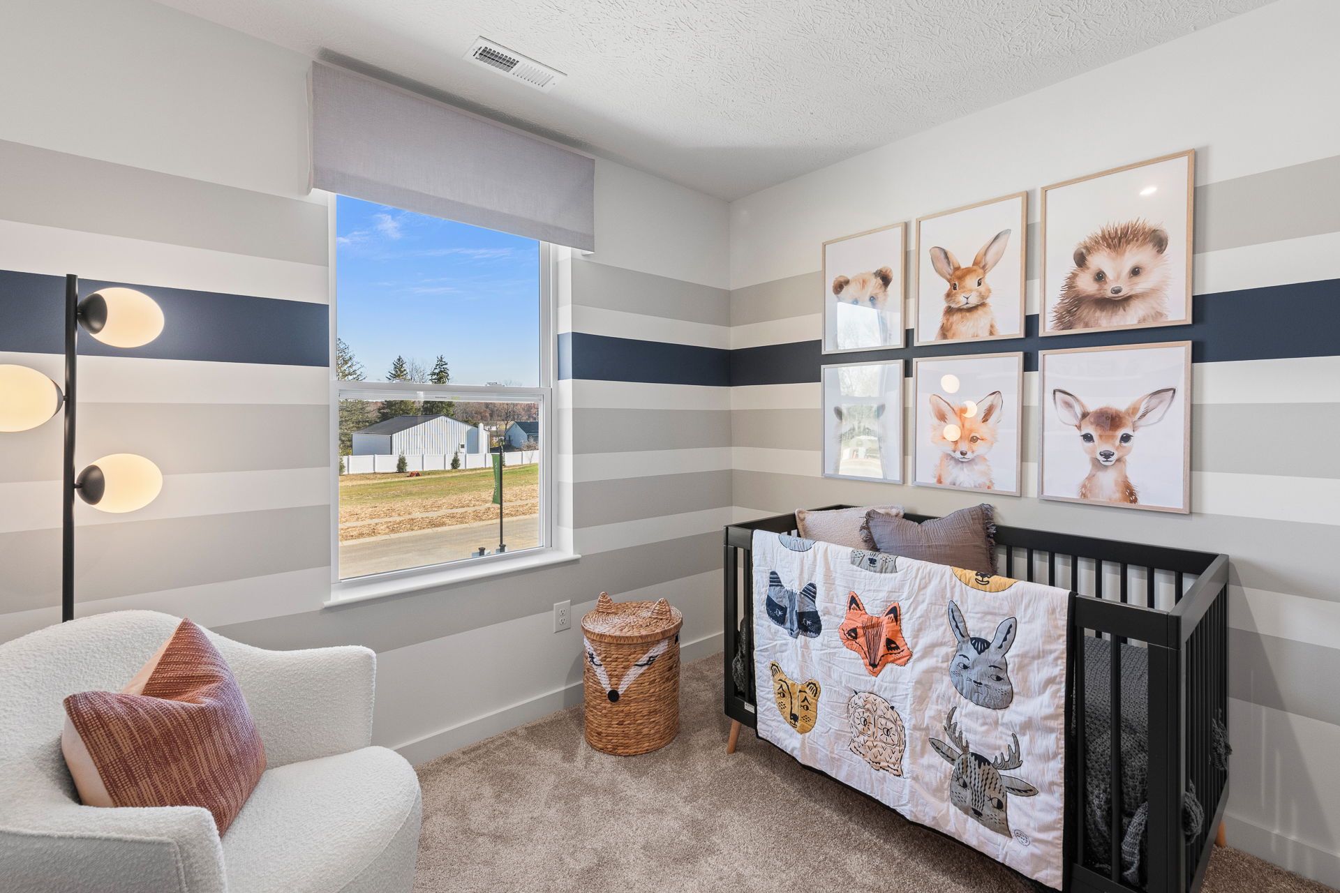 Modern nursery with animal-themed decor, featuring striped walls, framed animal prints, a cozy chair, and a crib with a nature-inspired quilt.