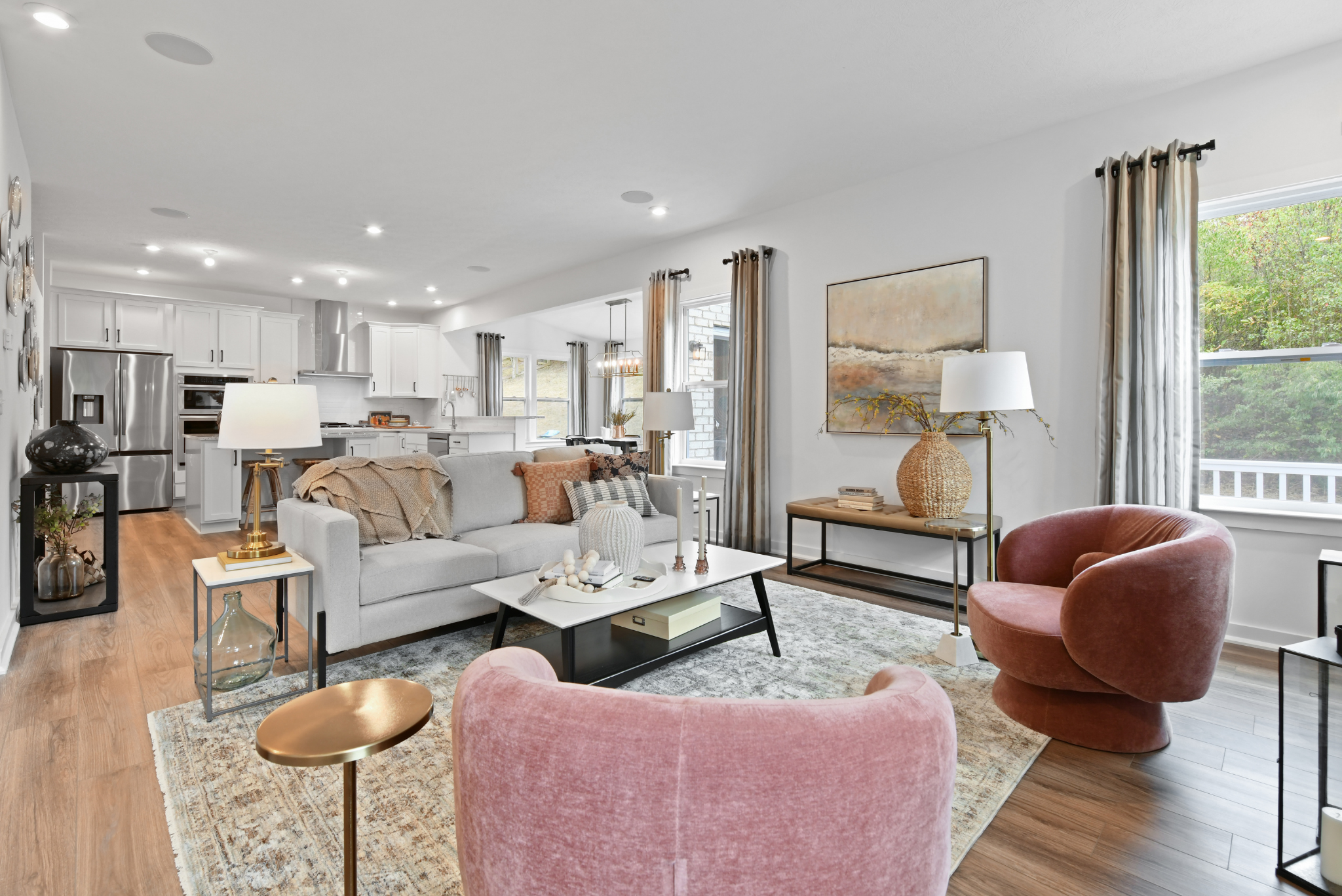 Modern open-concept living room and kitchen with stylish decor, featuring a gray sofa, pink chairs, and hardwood floors.