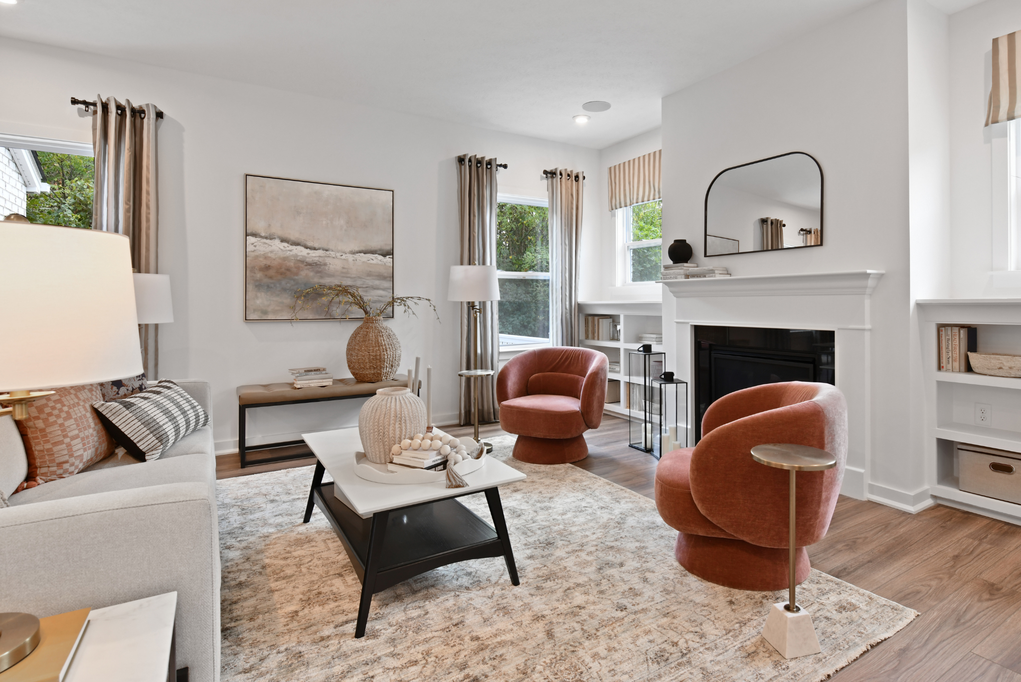 Modern living room with chic furnishings, featuring pink velvet chairs, a cozy fireplace, and stylish decor accents.