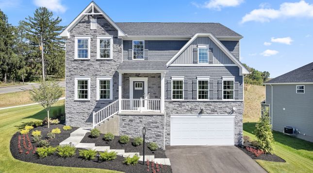Modern two-story stone house with manicured landscaping, white accents, and a two-car garage on a sunny day.