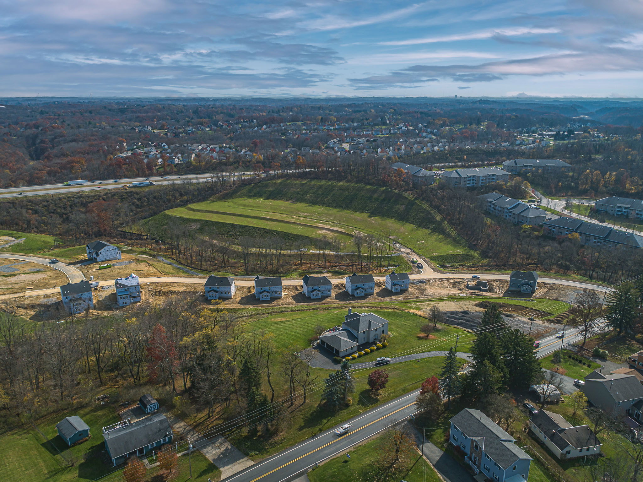 Aerial view of a suburban housing development under construction, surrounded by greenery and existing homes.