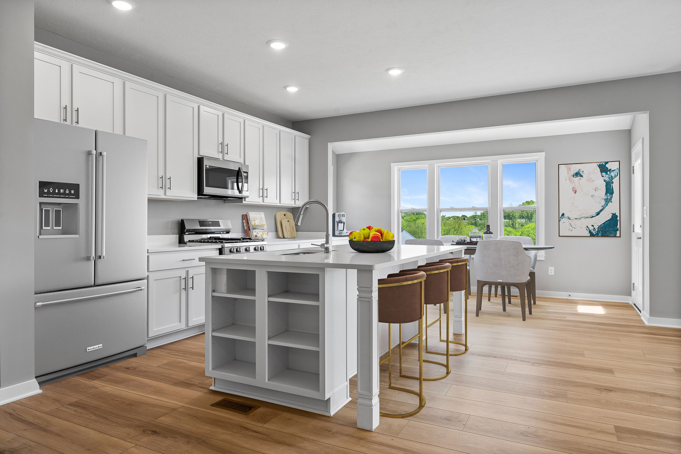 Modern kitchen with white cabinetry, stainless steel appliances, a central island with seating, and large windows offering natural light.