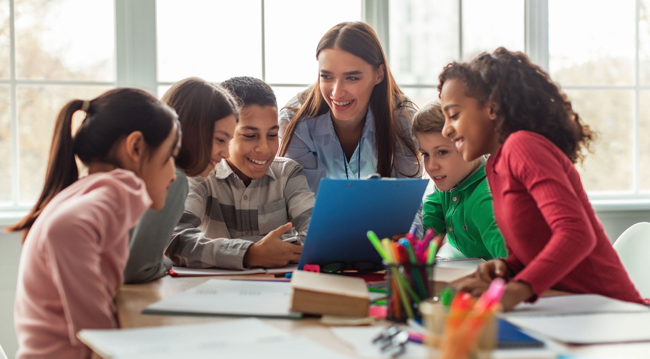A diverse group of school children engaged in collaborative learning with a teacher in a classroom setting.