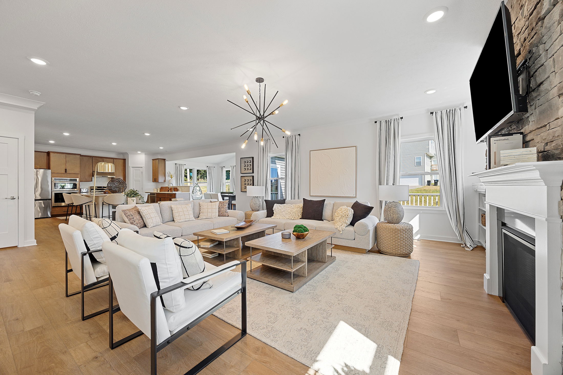 Modern open-concept living room and kitchen with contemporary furnishings, wood flooring, and a stylish chandelier.