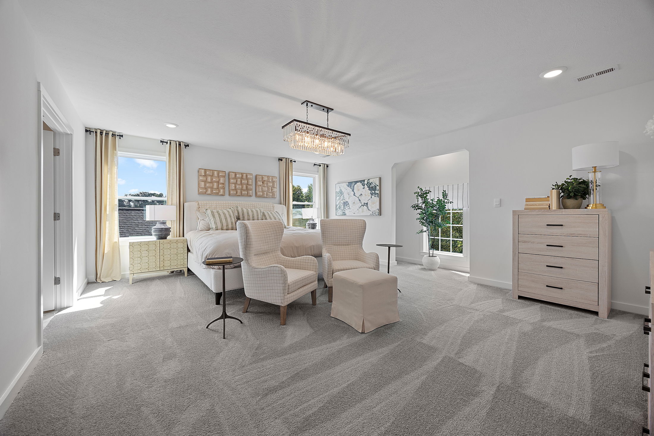 Modern, spacious bedroom with elegant decor, featuring a chandelier, plush seating area, and large windows with abundant natural light.